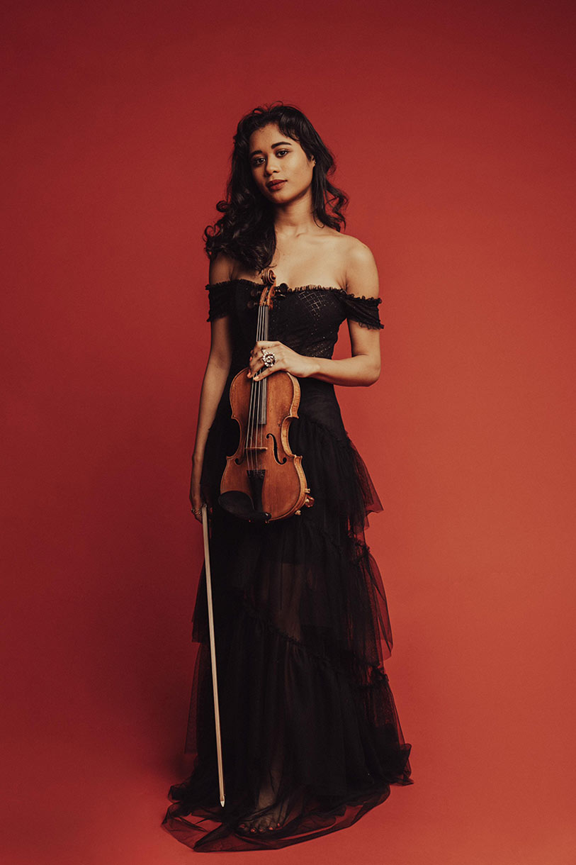 Woman in black dress holding a violin against a red background.