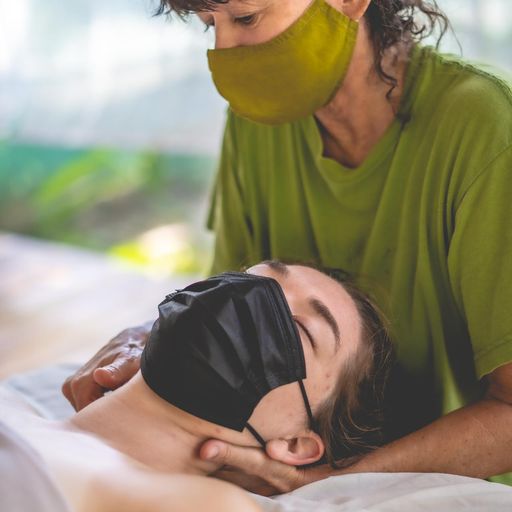 Person receiving care from another person, both wearing face masks, in a close-up scene.