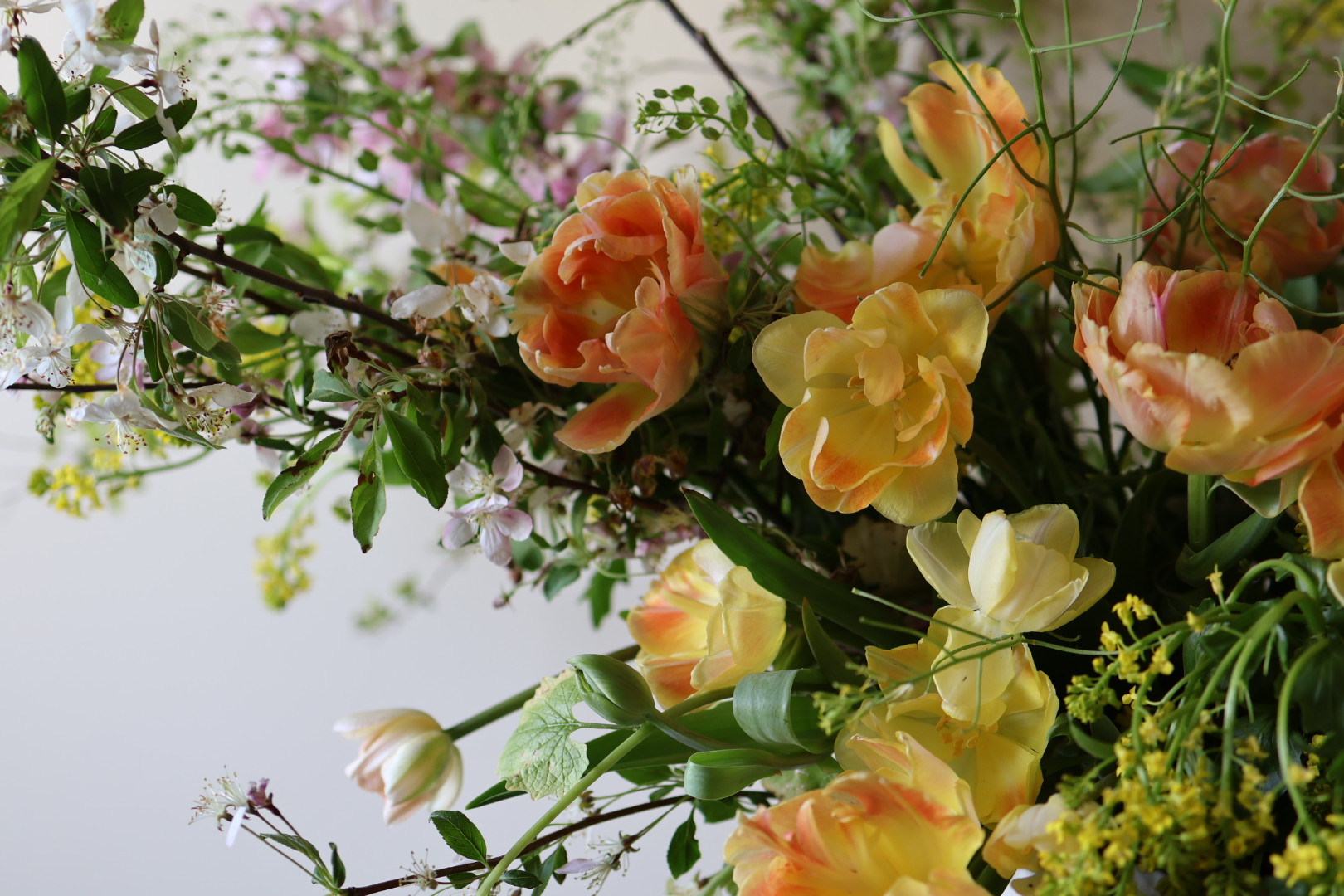 Arrangement of peach, yellow, and white flowers with green foliage and small purple and yellow accents.