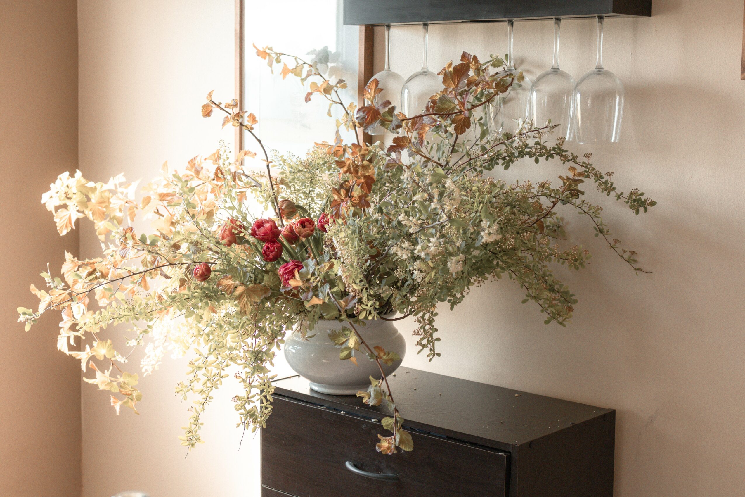 Large flower arrangement in a white vase on a black cabinet, with sunlight streaming in from the left.