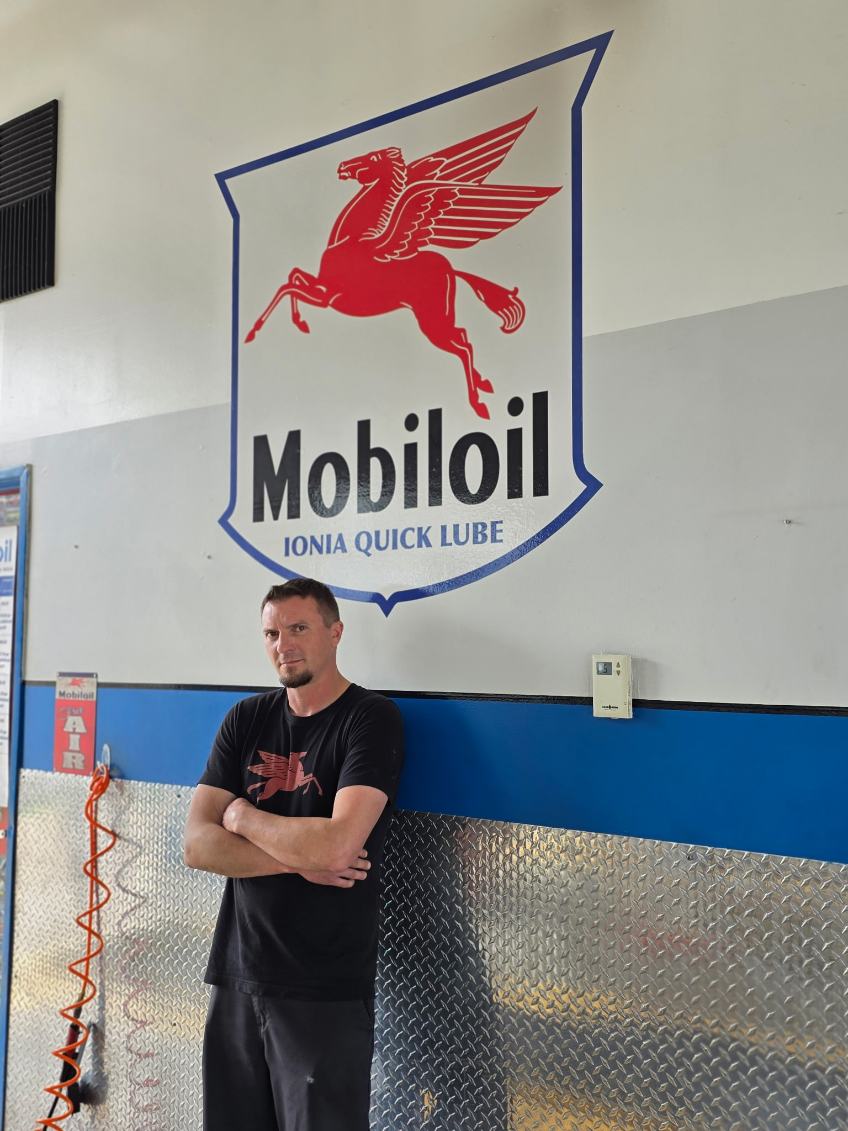 Man standing with arms crossed in front of a wall with Mobil 1 logo and blue stripe.