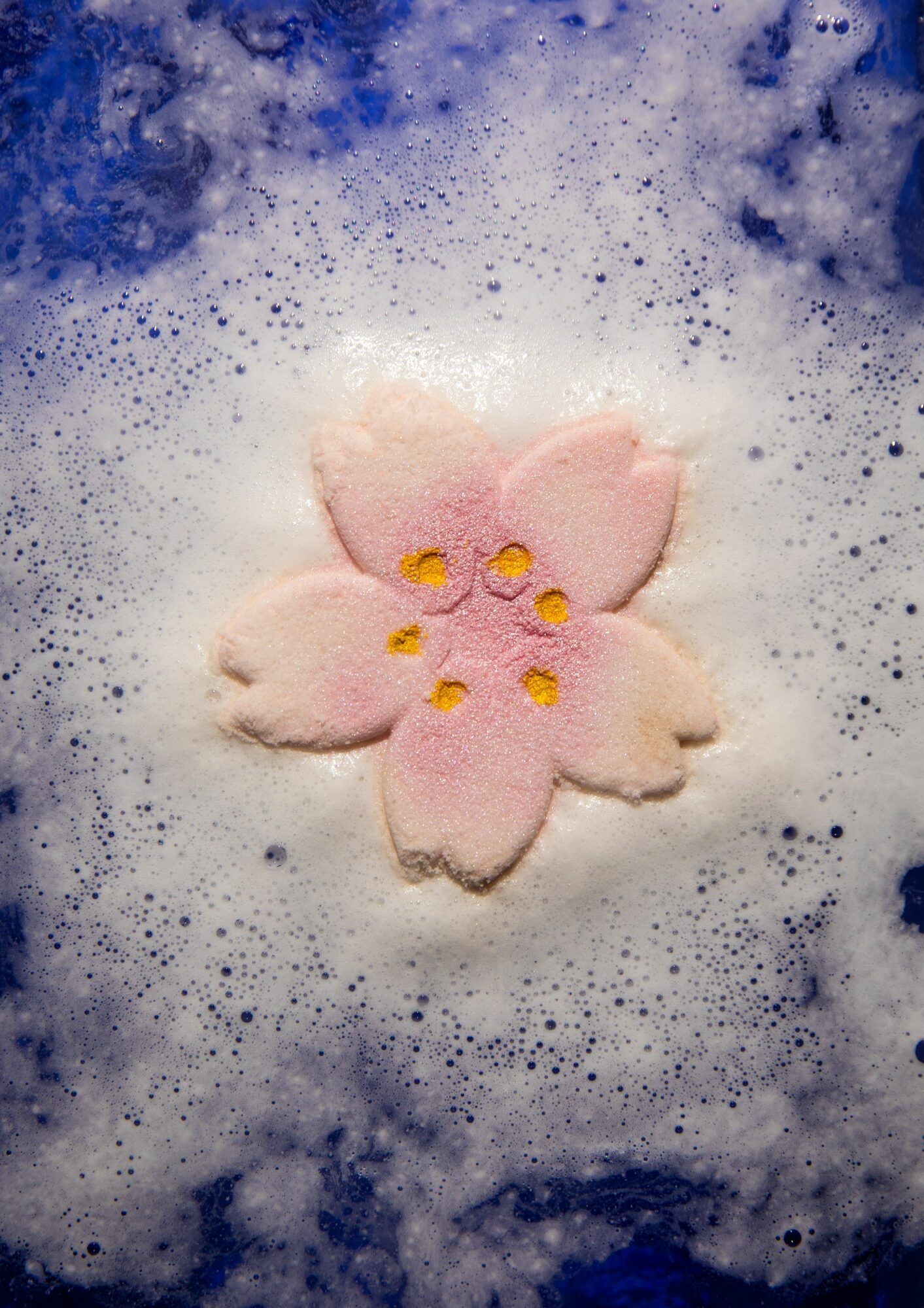 Pink flower-shaped object with yellow details in soapy foam, surrounded by blue and white bubbles.