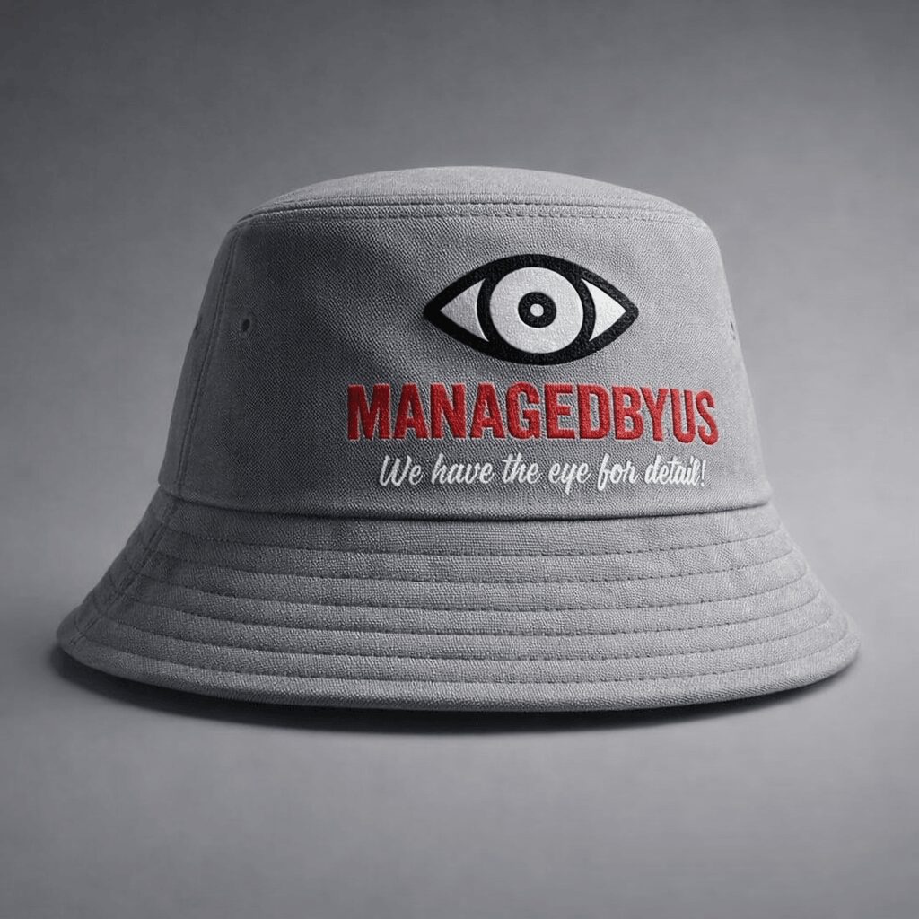 Gray bucket hat with eye logo, red text 'MANAGEDBYUS', and white slogan, on gray background.
