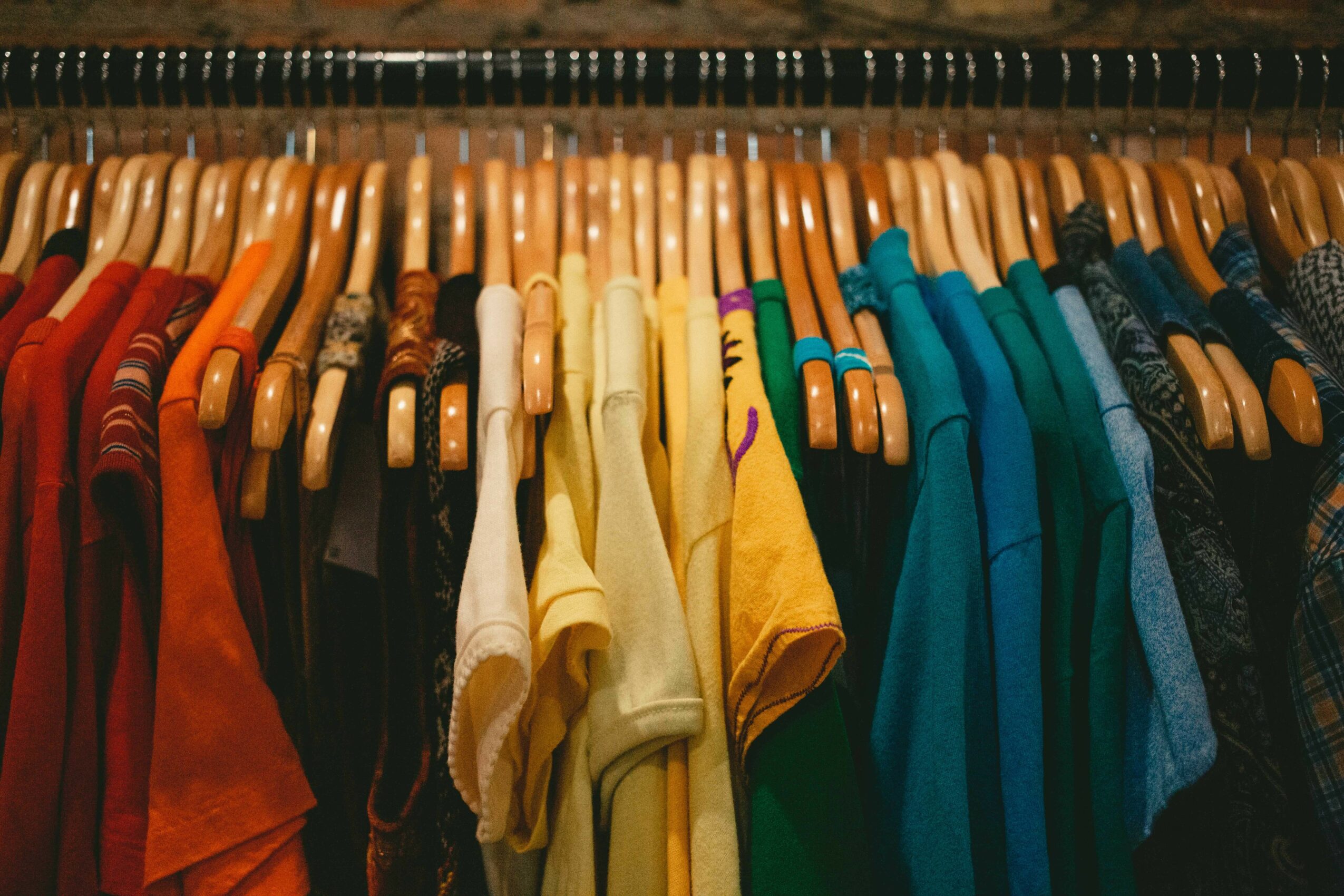 Clothes hanging on a rack, organized by color from red to blue, with various shirts and garments visible.