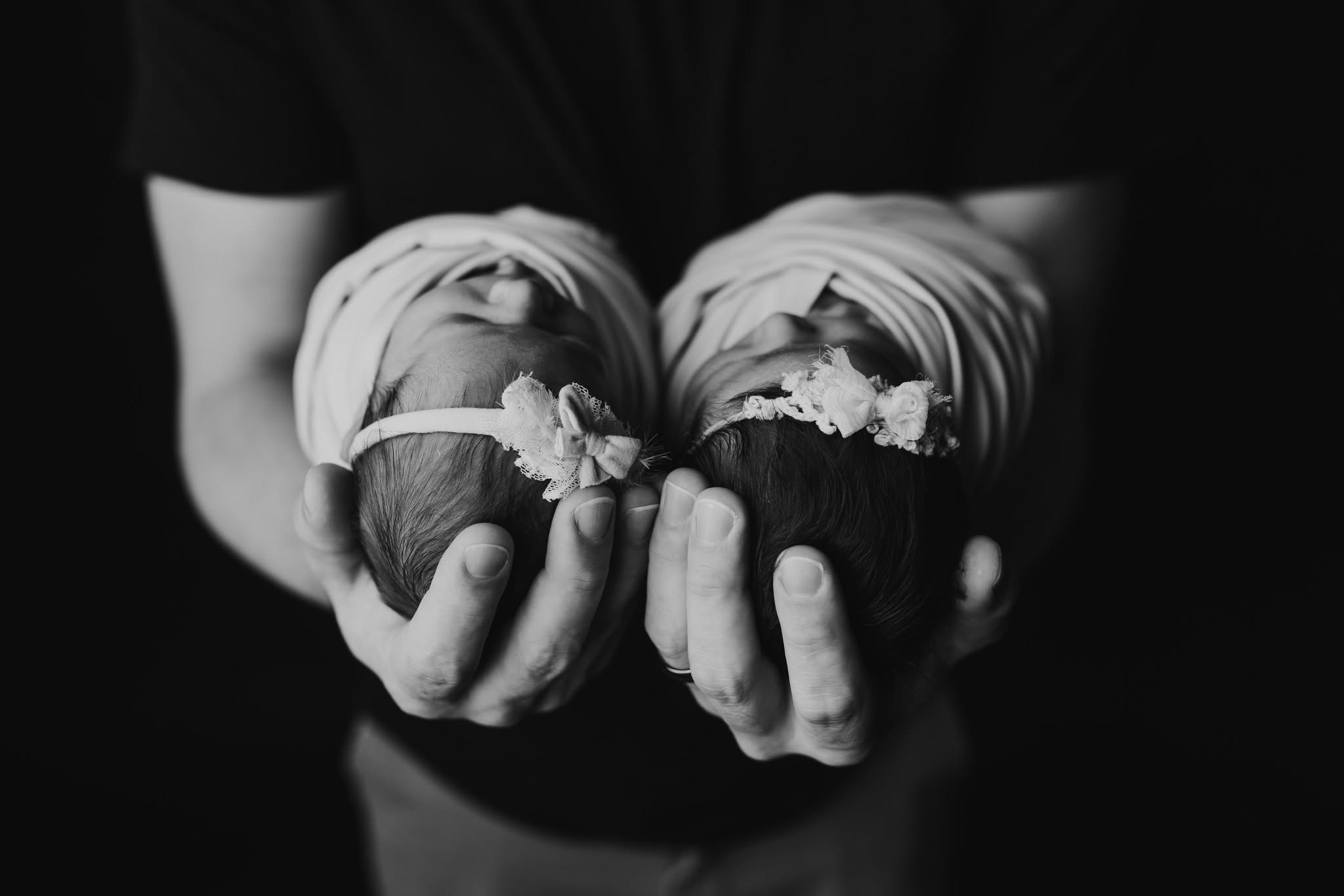 Person holding two wrapped babies, one in each hand, with a dark background, black and white photo.