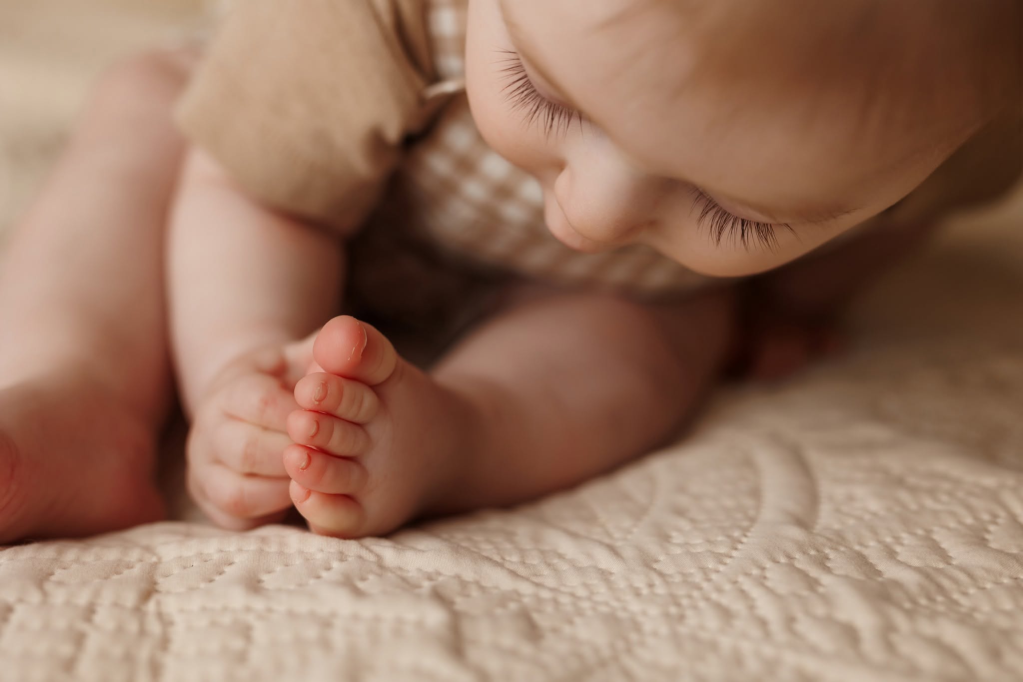 Close-up of a young child's face and hand, lying on a textured surface, with soft lighting.