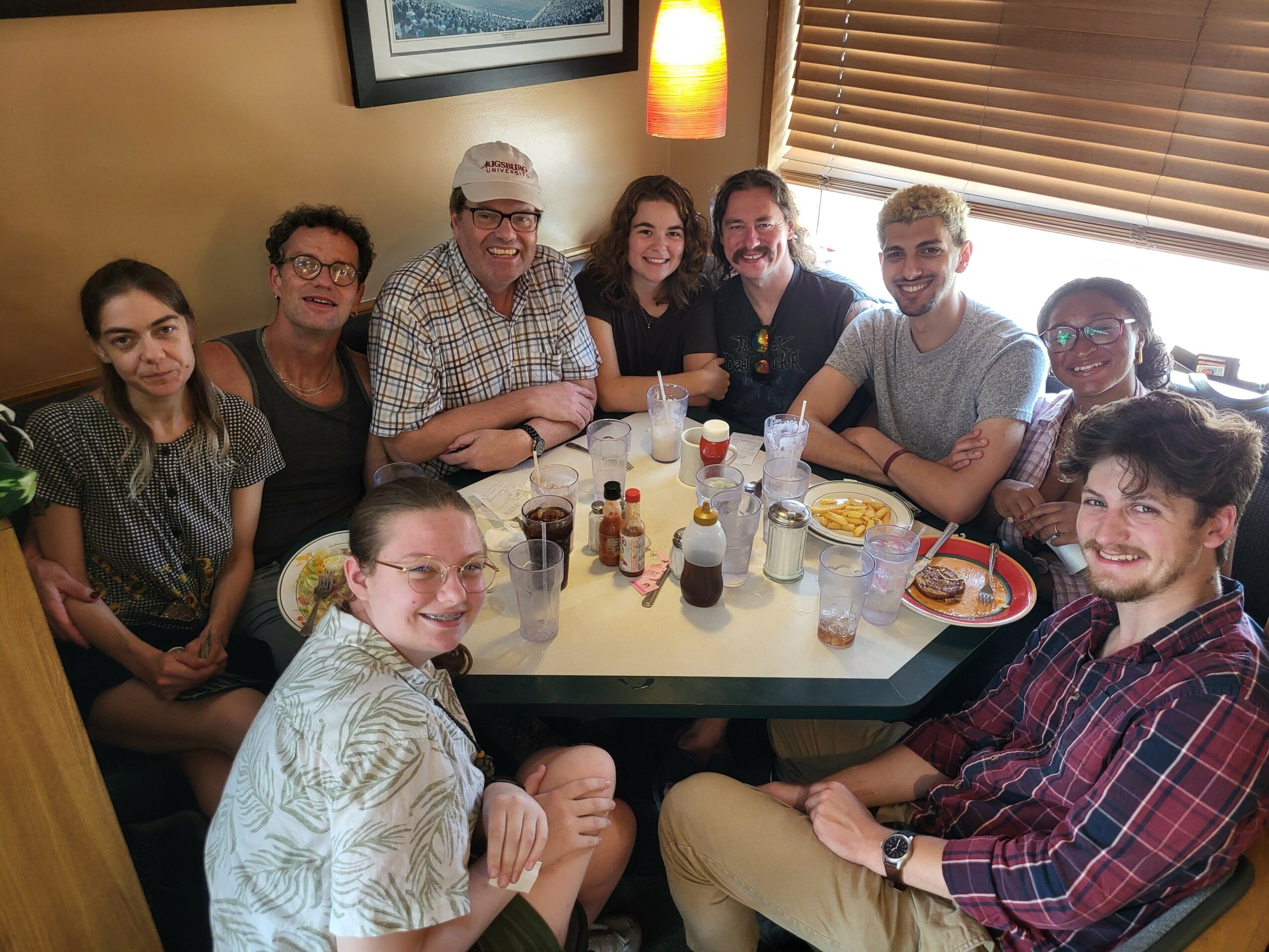 Group of ten people sitting around a table in a restaurant, smiling, with drinks and food on the table.