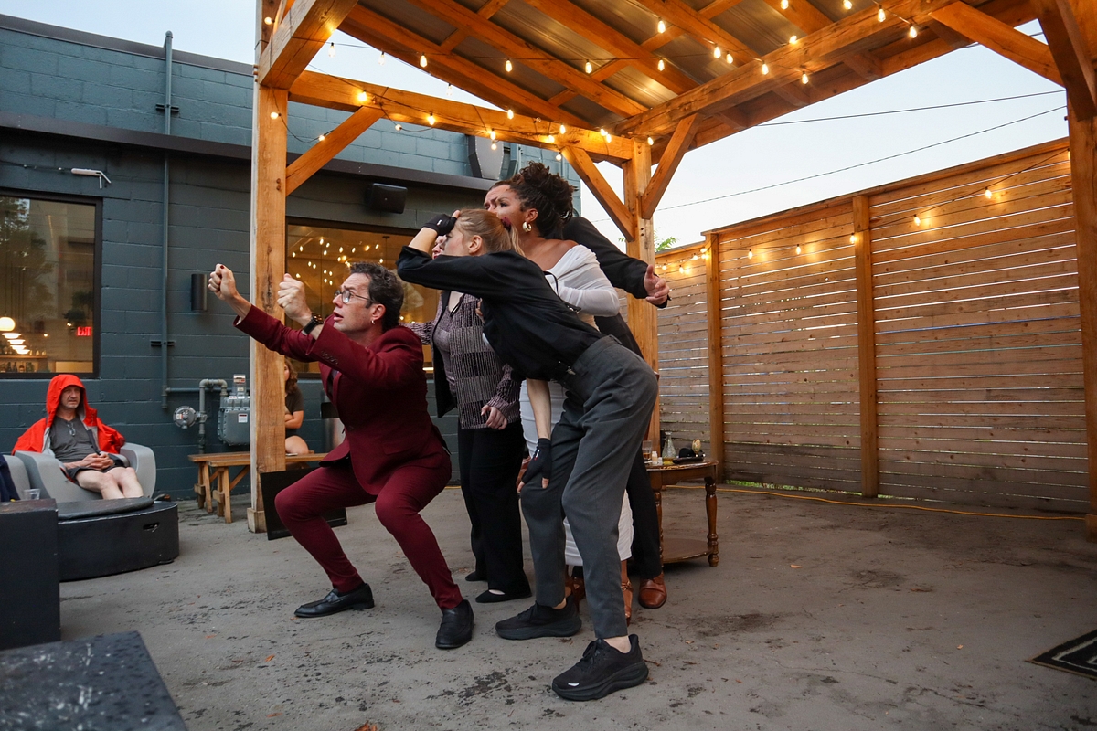 Group of people dancing under a wooden pergola outdoors at dusk, with a person sitting on a couch nearby.