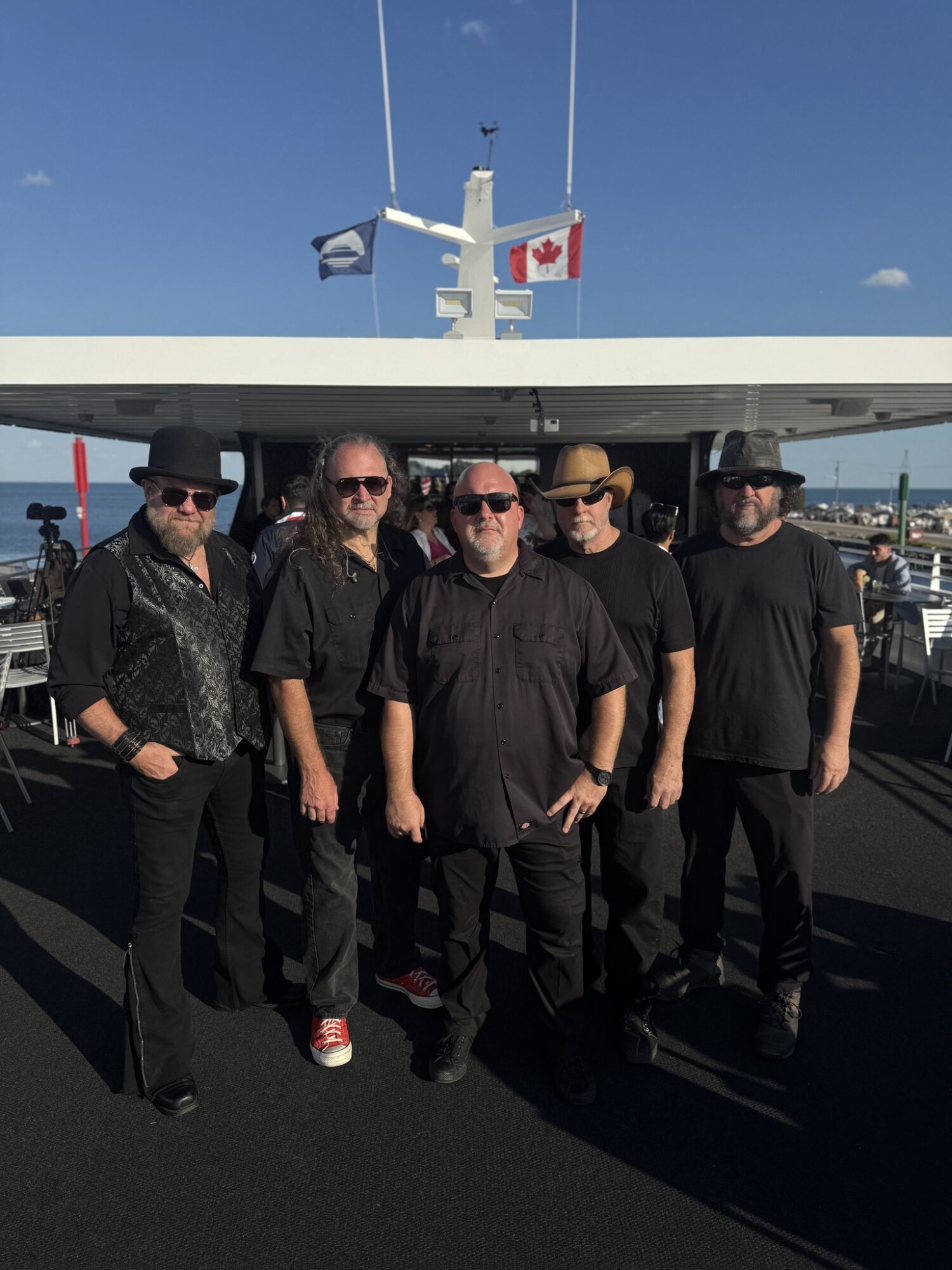 Five men stand together on a boat deck with flags, including Canada and a blue flag, in the background.