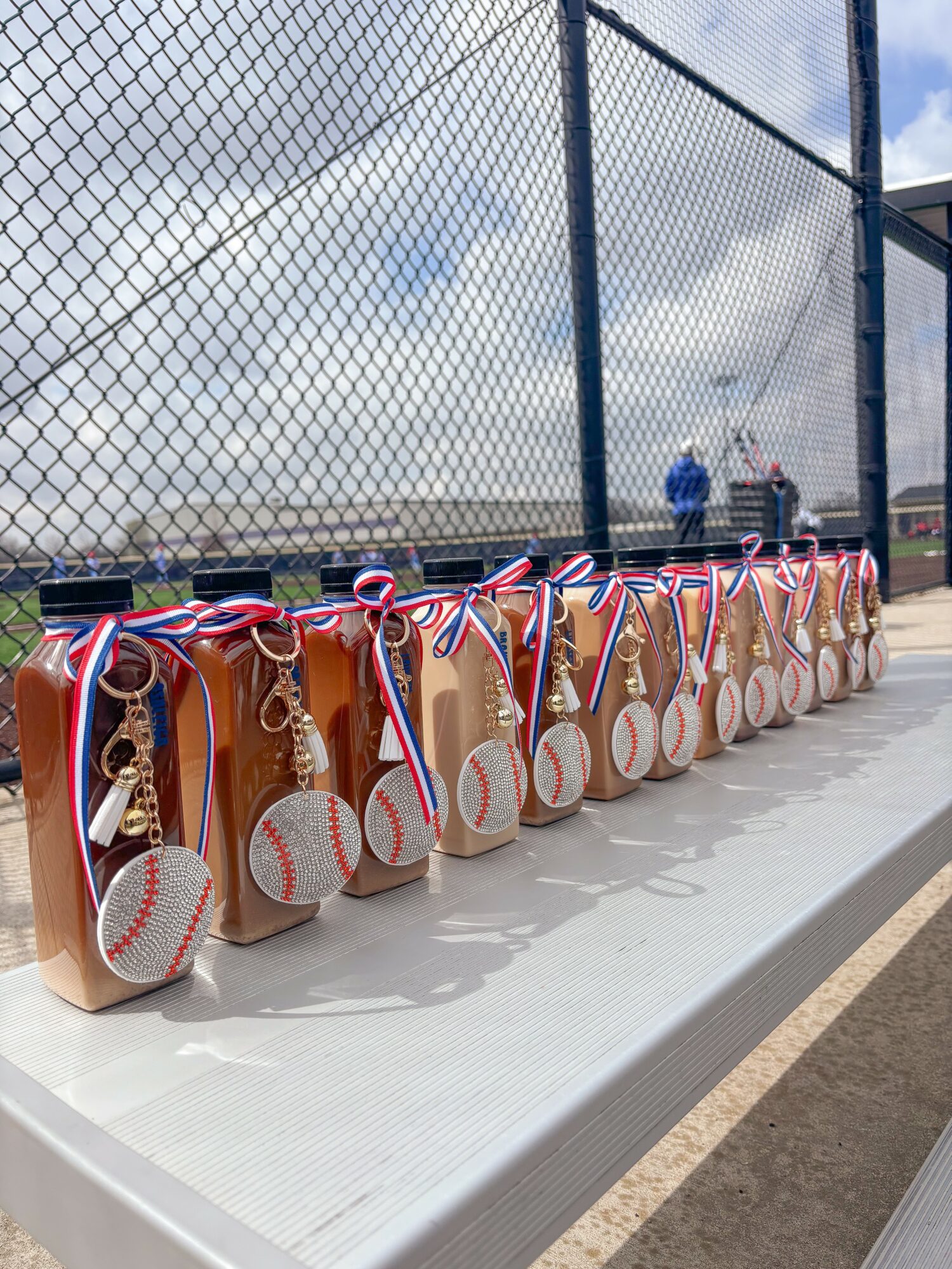 Row of medals with ribbons and small basketballs on a table at a sports event, with a fence and sky in background.