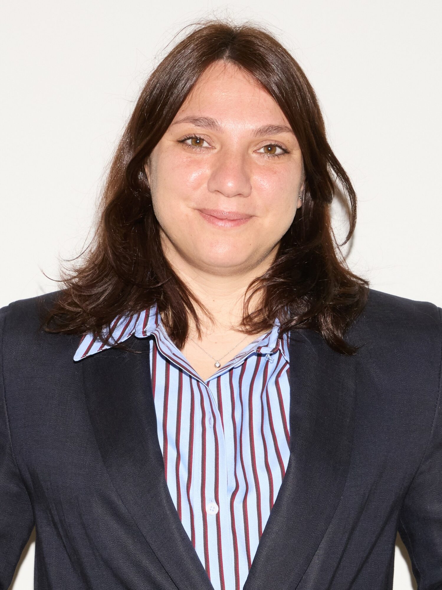 Young woman with shoulder-length dark hair, wearing a striped shirt and dark blazer, smiling at the camera.