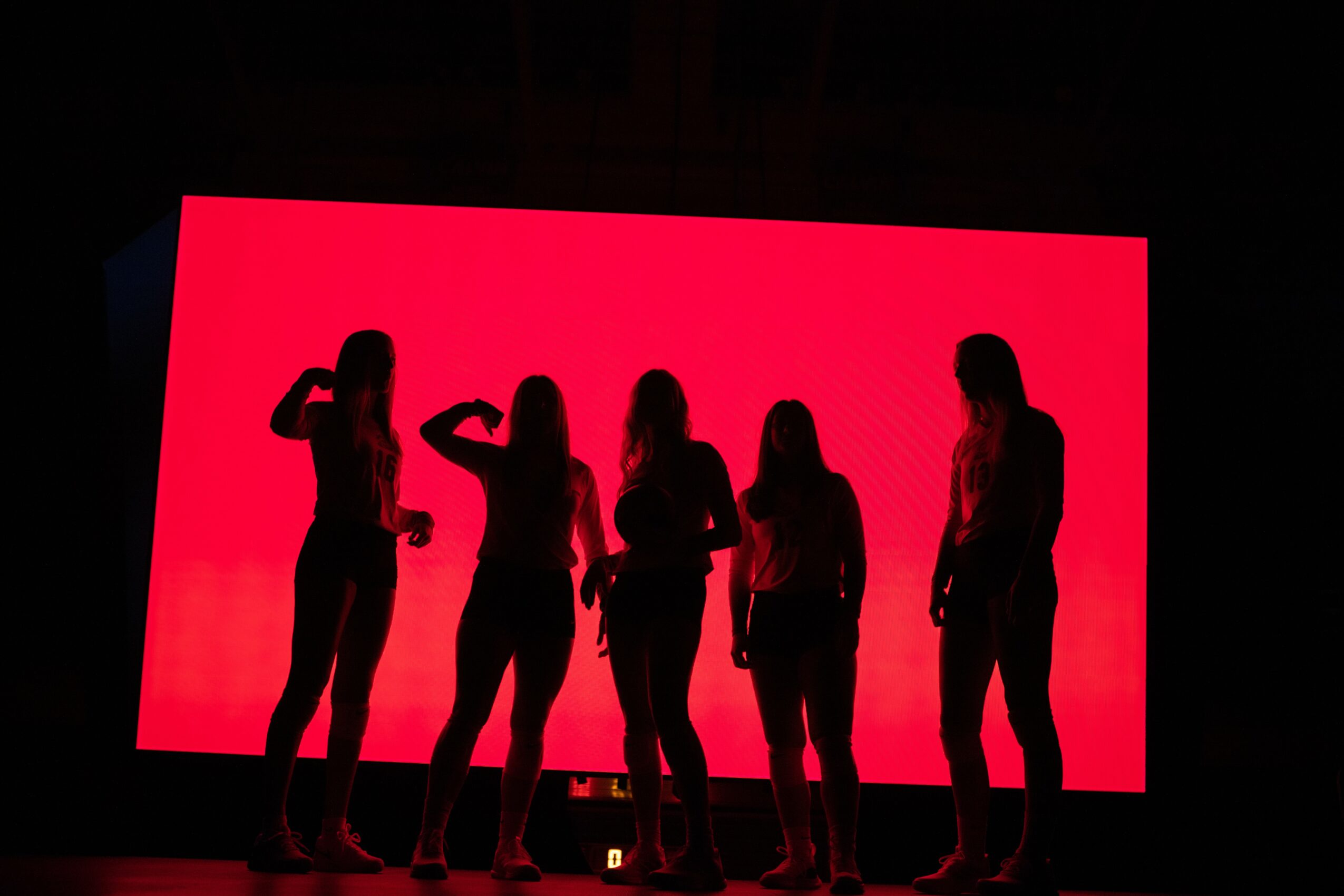 Five people stand in front of a large red screen, silhouetted against the bright background.