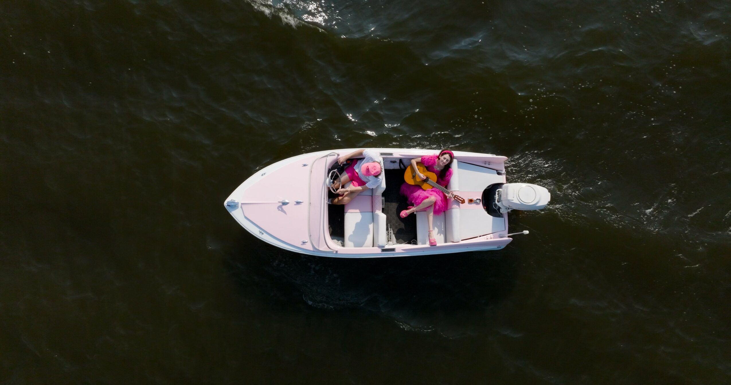 Two people sit in a small boat on dark water, viewed from above.
