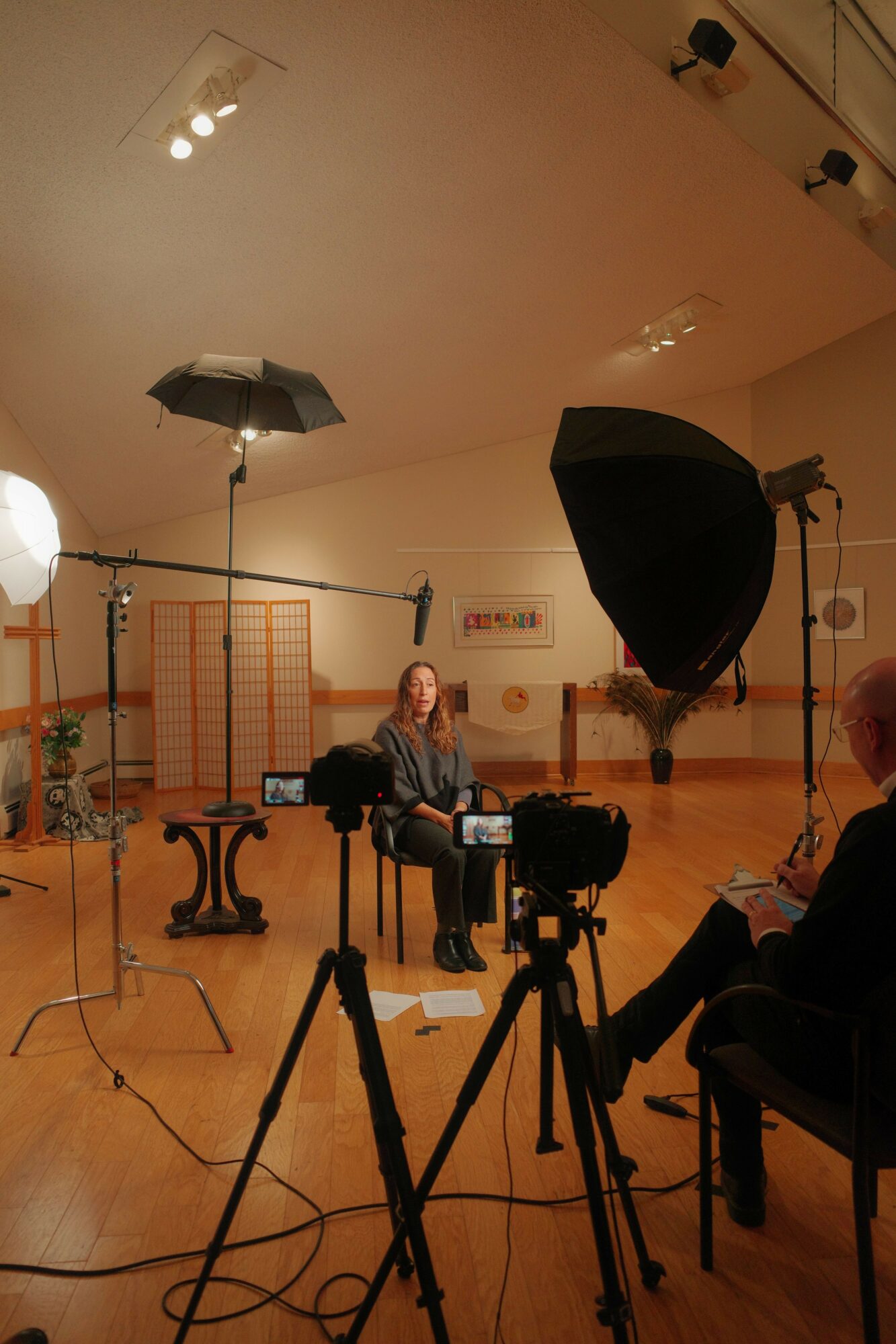 Person sitting on a chair in a studio with lighting equipment and a wooden floor.