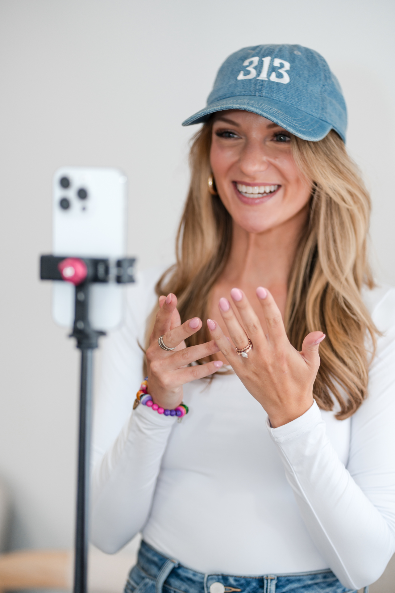 Woman smiling and talking to a camera on a tripod, wearing a blue cap and white top.