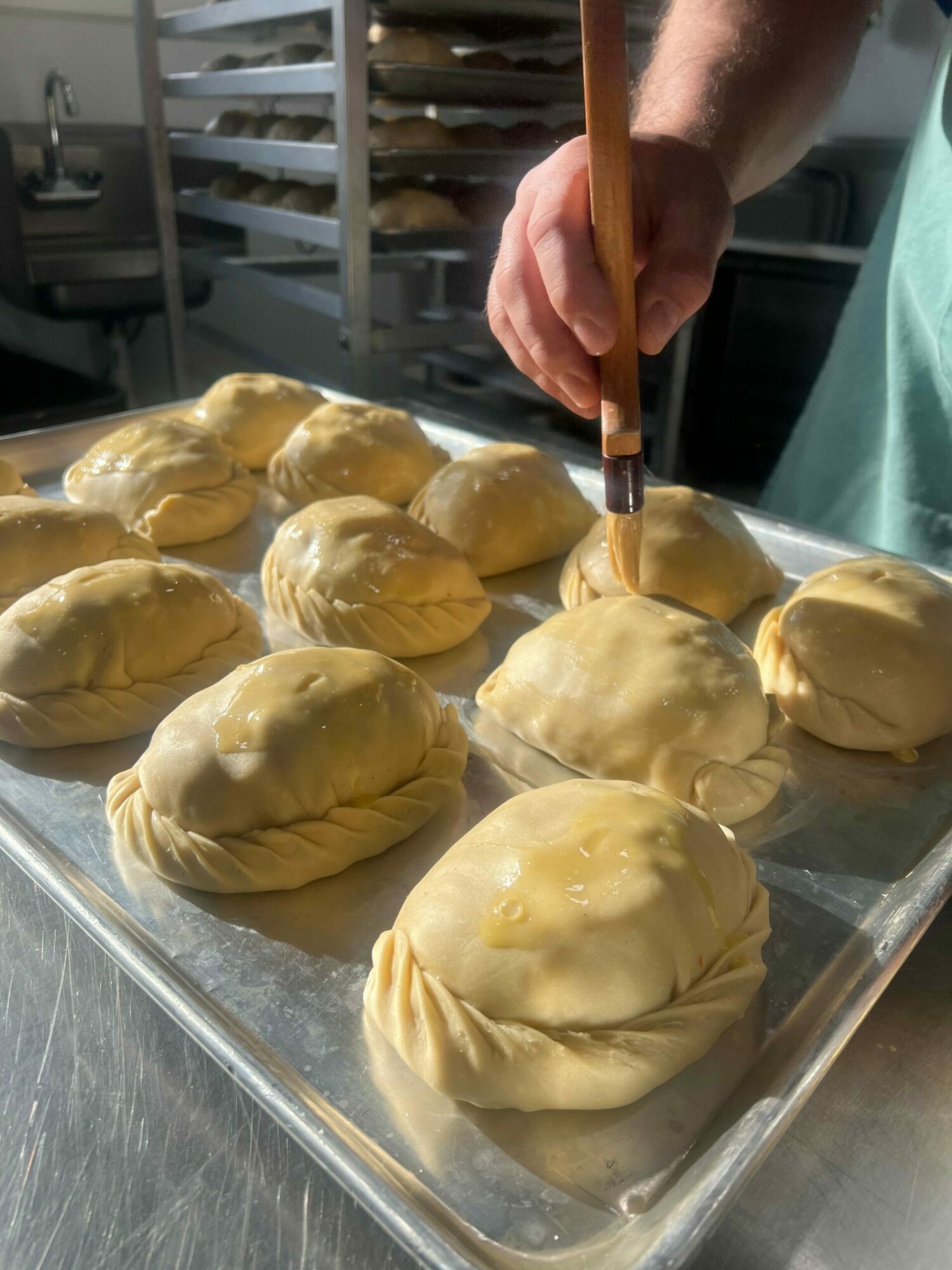 Person filling pastry with filling using a piping bag on a baking tray with unbaked pastries.