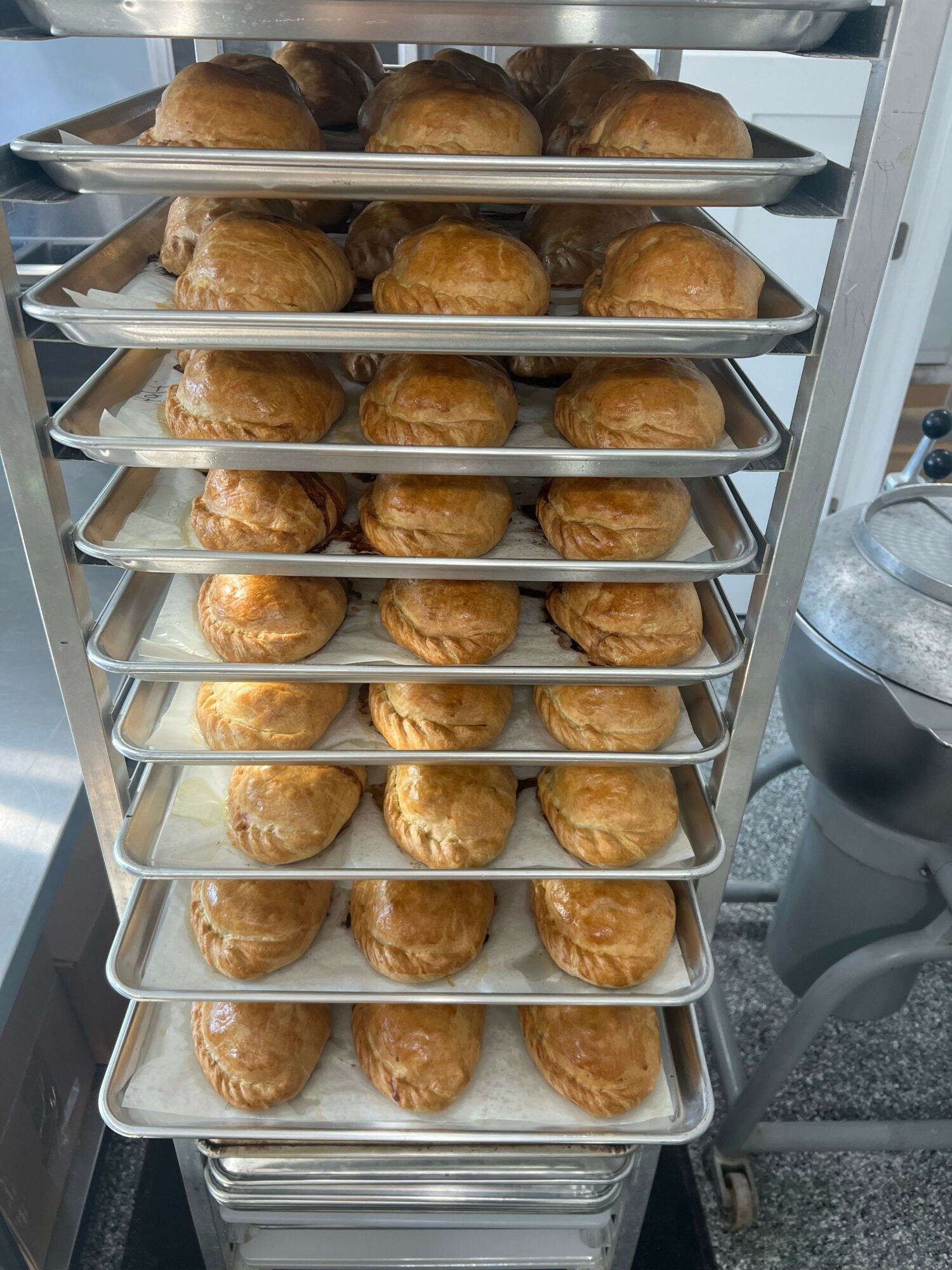 Multiple cream puffs arranged on a metal cooling rack, cooling on a countertop, with a container in the background.