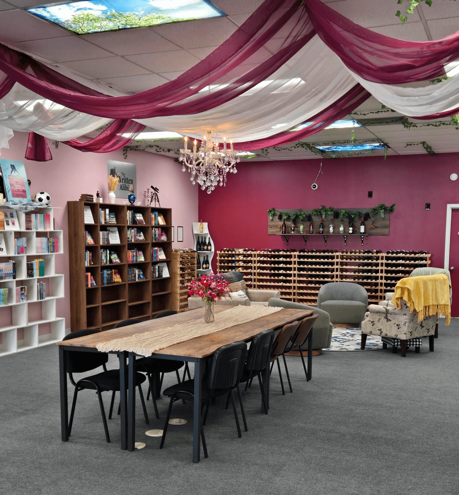 Room with pink walls, decorated ceiling with pink and white drapes, chandelier, bookshelves, table with flowers, and seating area.