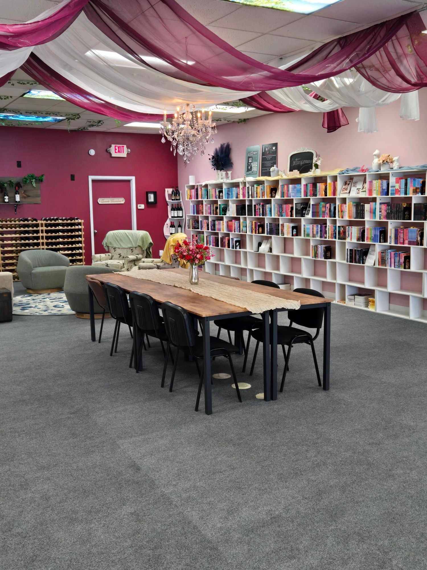 Room with pink and white walls, bookshelf, table, and chairs, with a gray carpeted floor.
