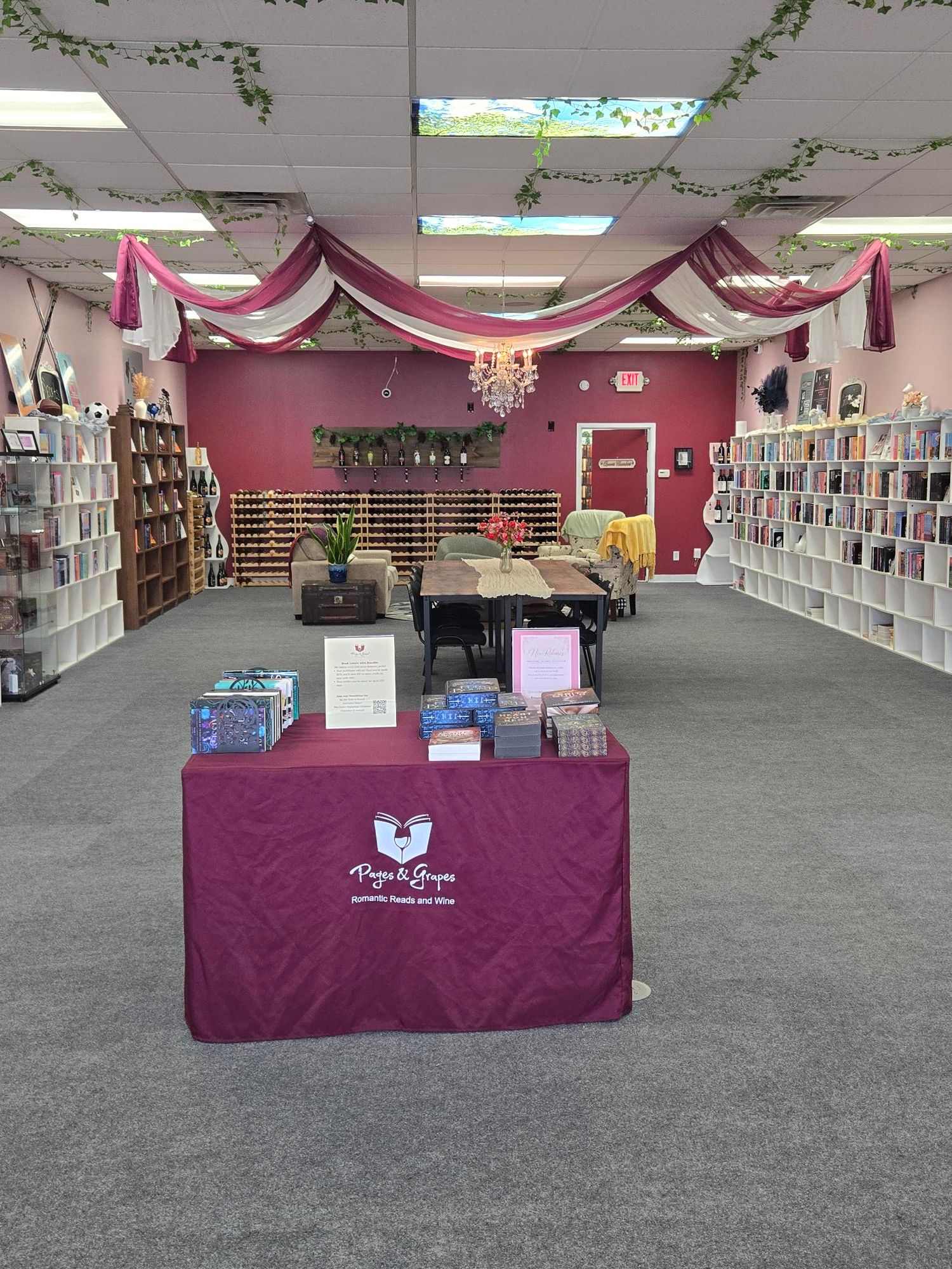 Indoor space with pink and white decor, shelves with books or products, and a table with promotional items.