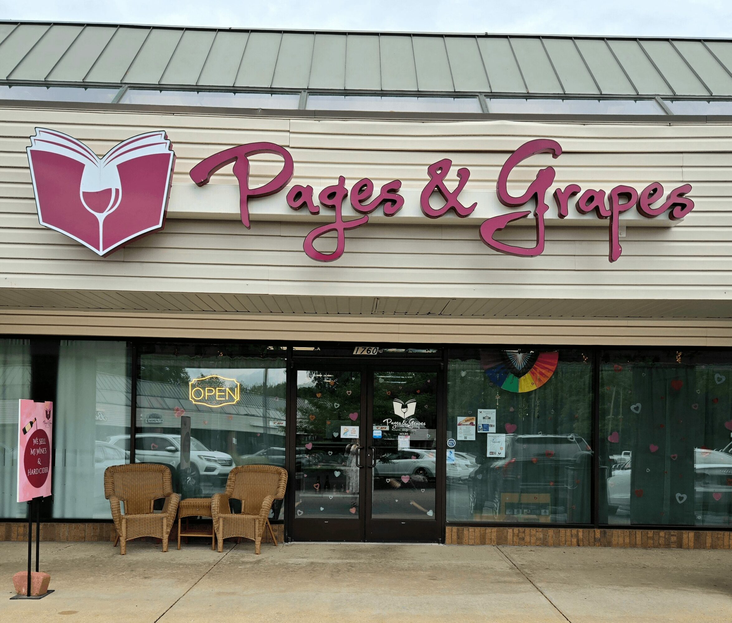 Storefront with sign reading 'Pages & Grapes' and a book and wine glass logo, glass windows, and chairs outside.