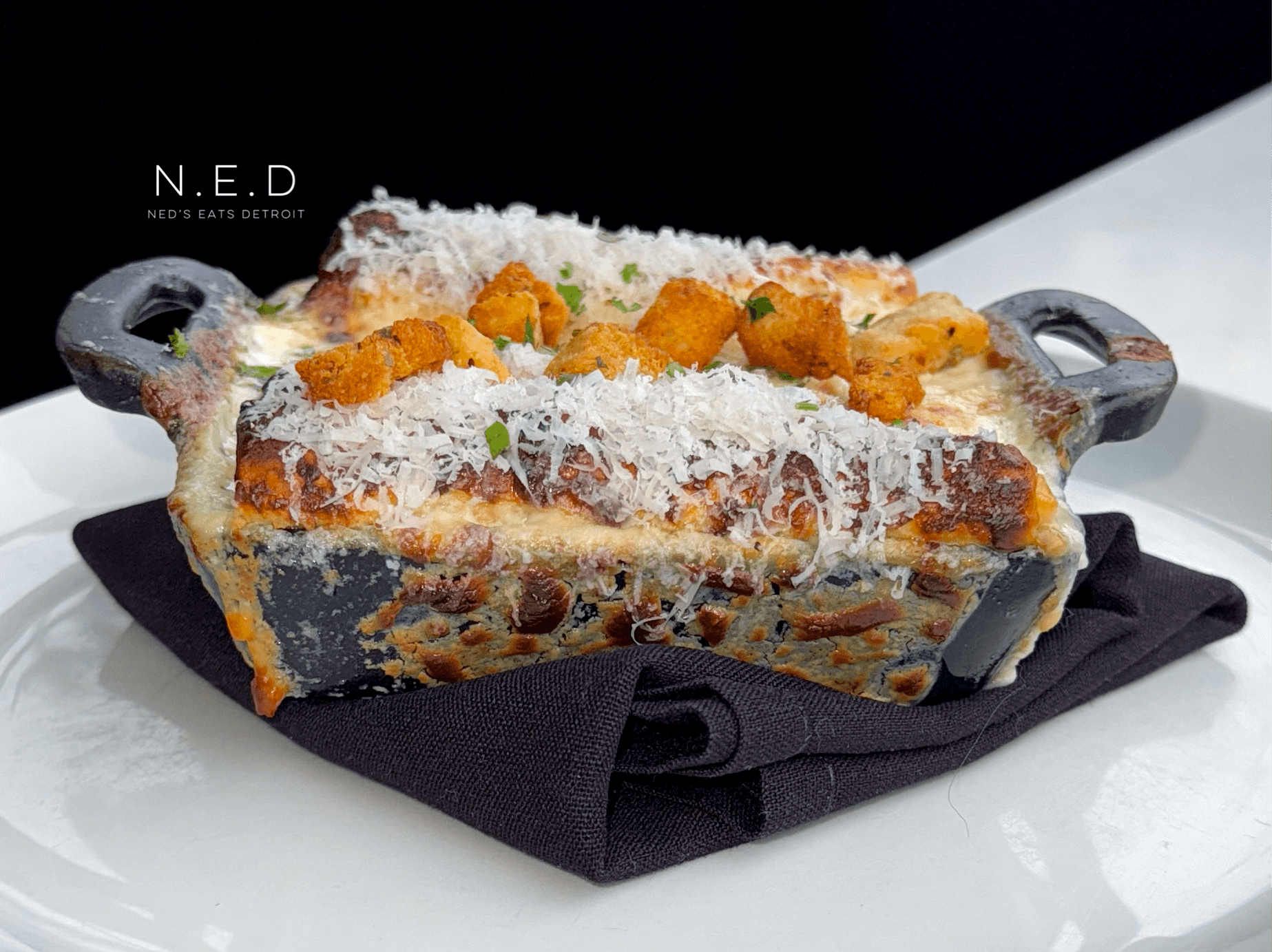 Baked dish with cheese, vegetables, and sauce in a black rectangular dish on a black cloth, on a white surface.