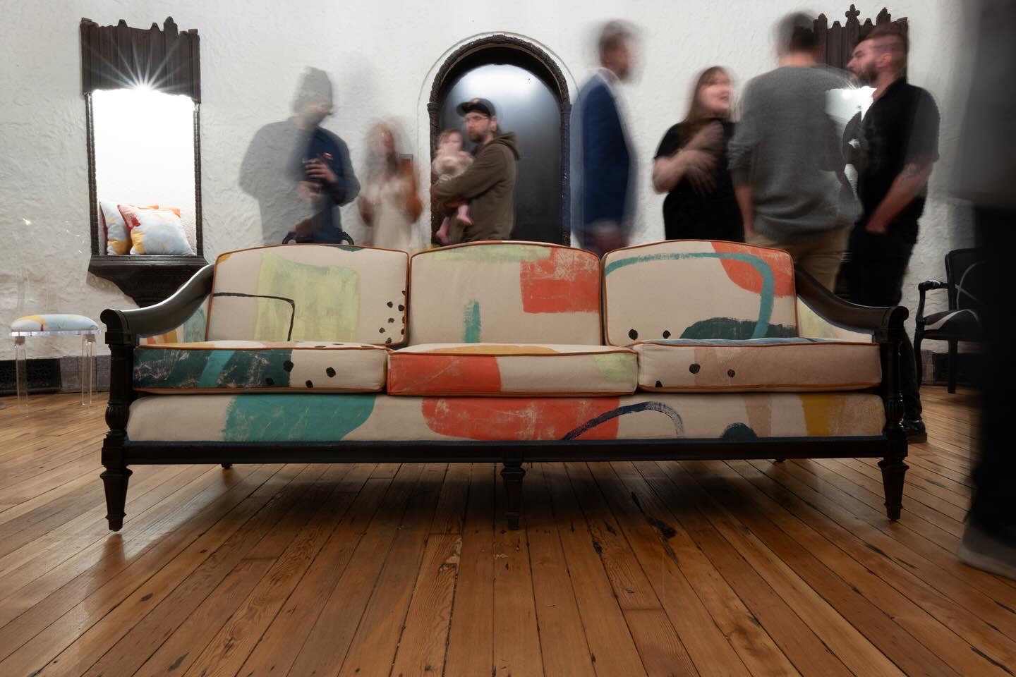 Colorful sofa with a black metal frame in a room with wooden floor and blurred people in the background.