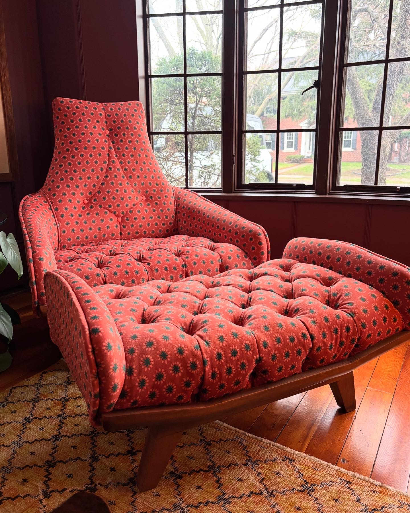 Upholstered armchair with matching ottoman, both with red fabric and black polka dots, placed near large window with view outside.