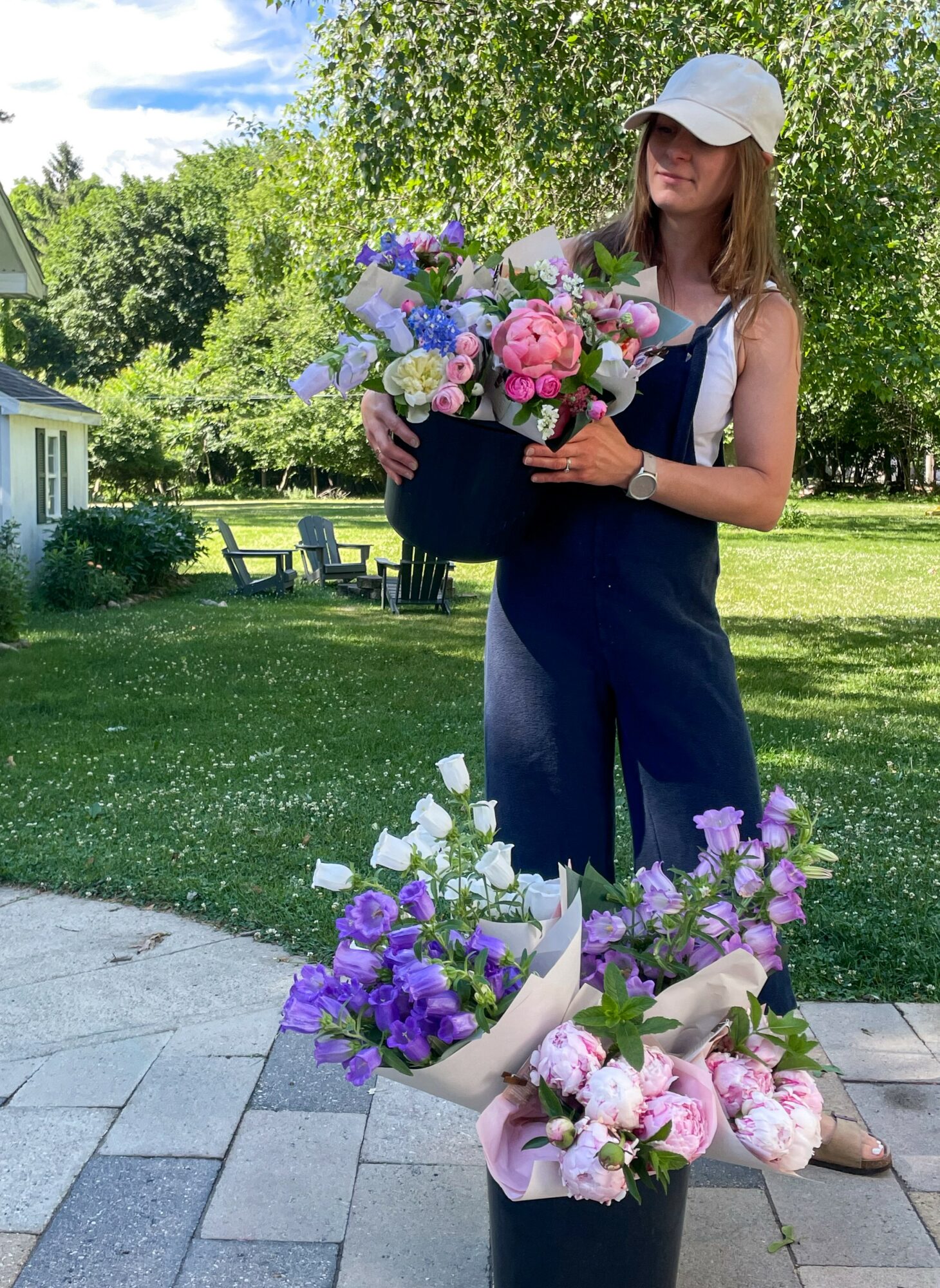 Woman holding a large bouquet of colorful flowers outdoors on a sunny day, with trees and a lawn in the background.