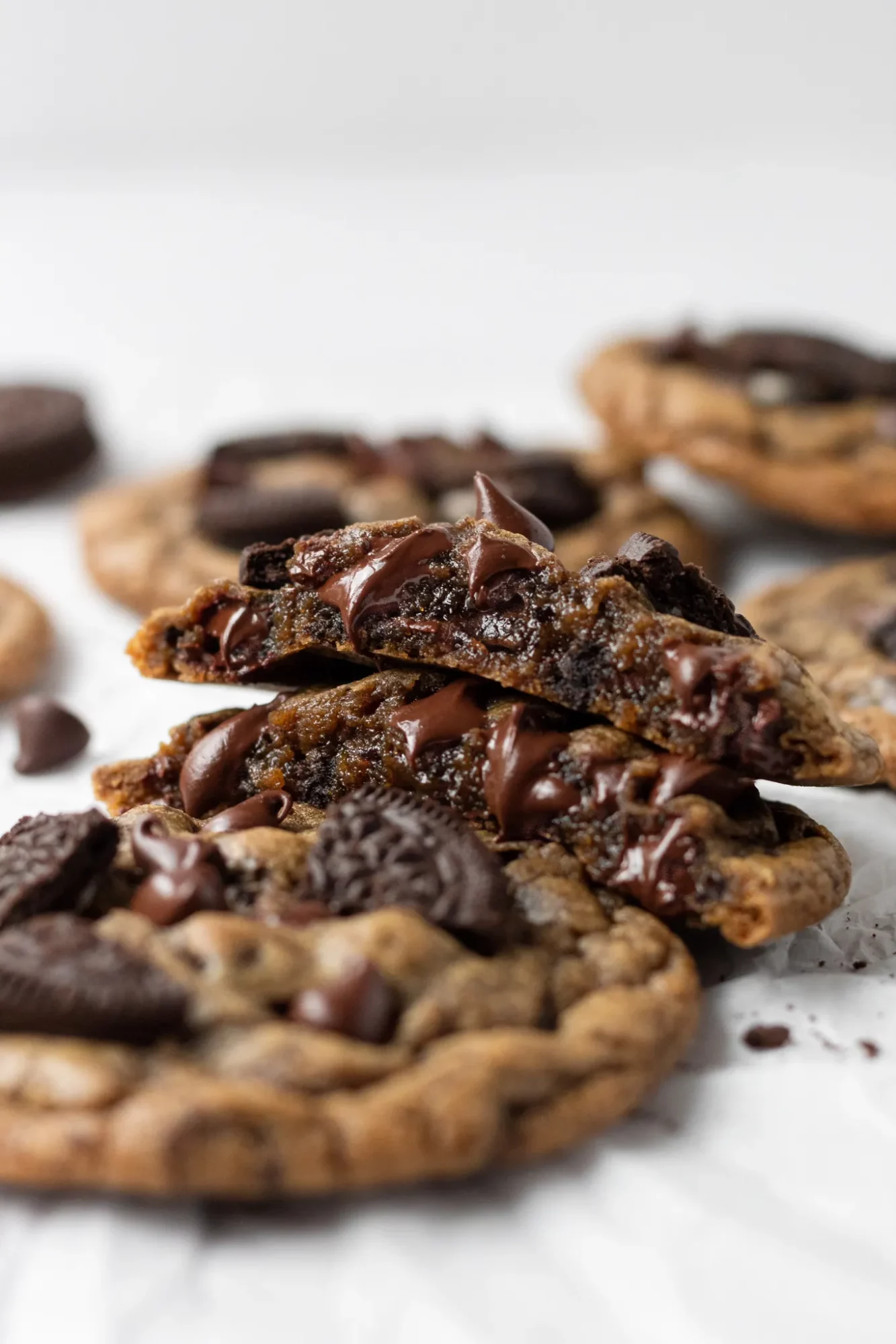 Close-up of chocolate chip cookies with melted chocolate, some broken, on a white surface.