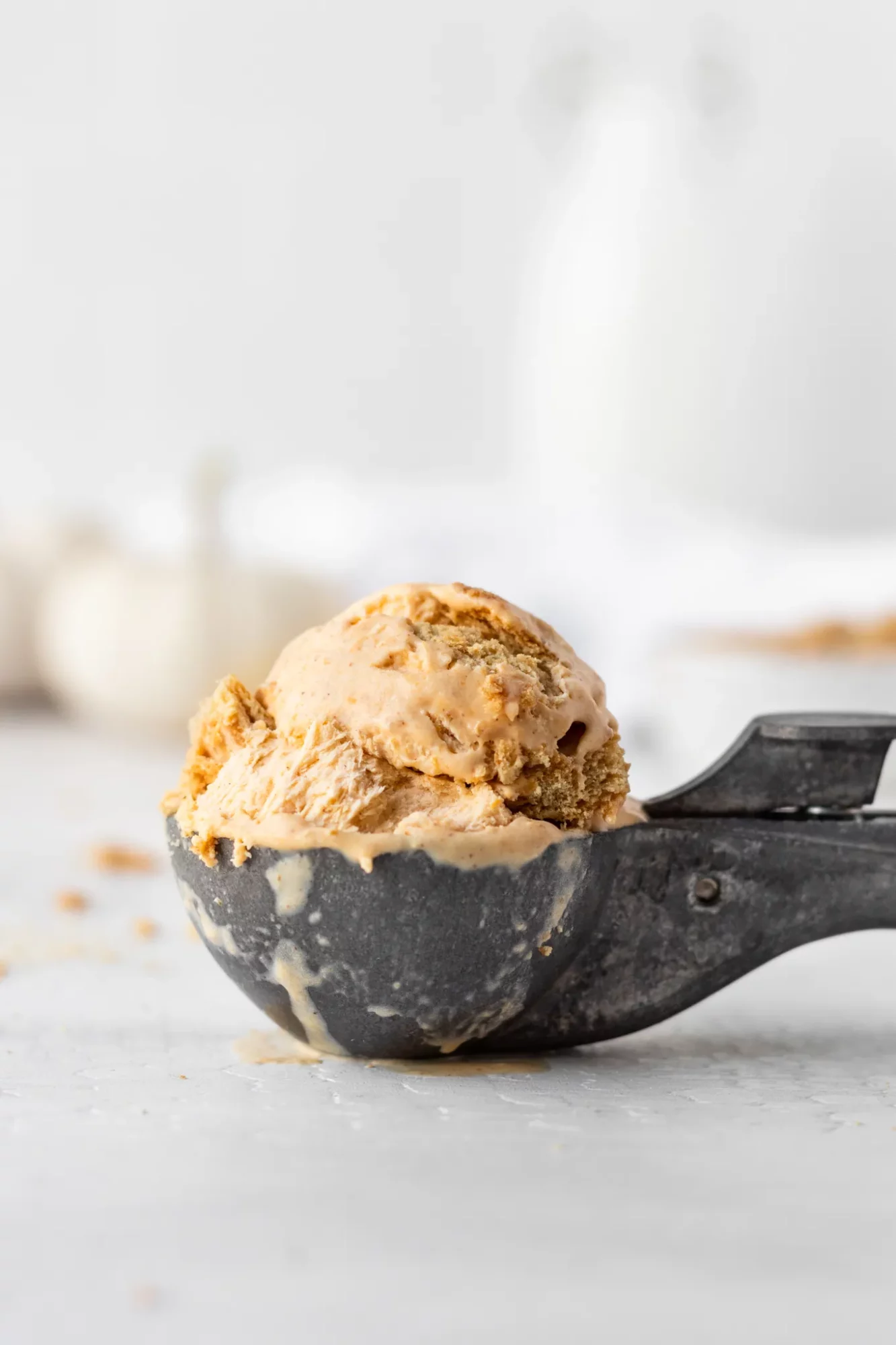 Scoops of ice cream in a black scoop on a white surface with a blurred background.