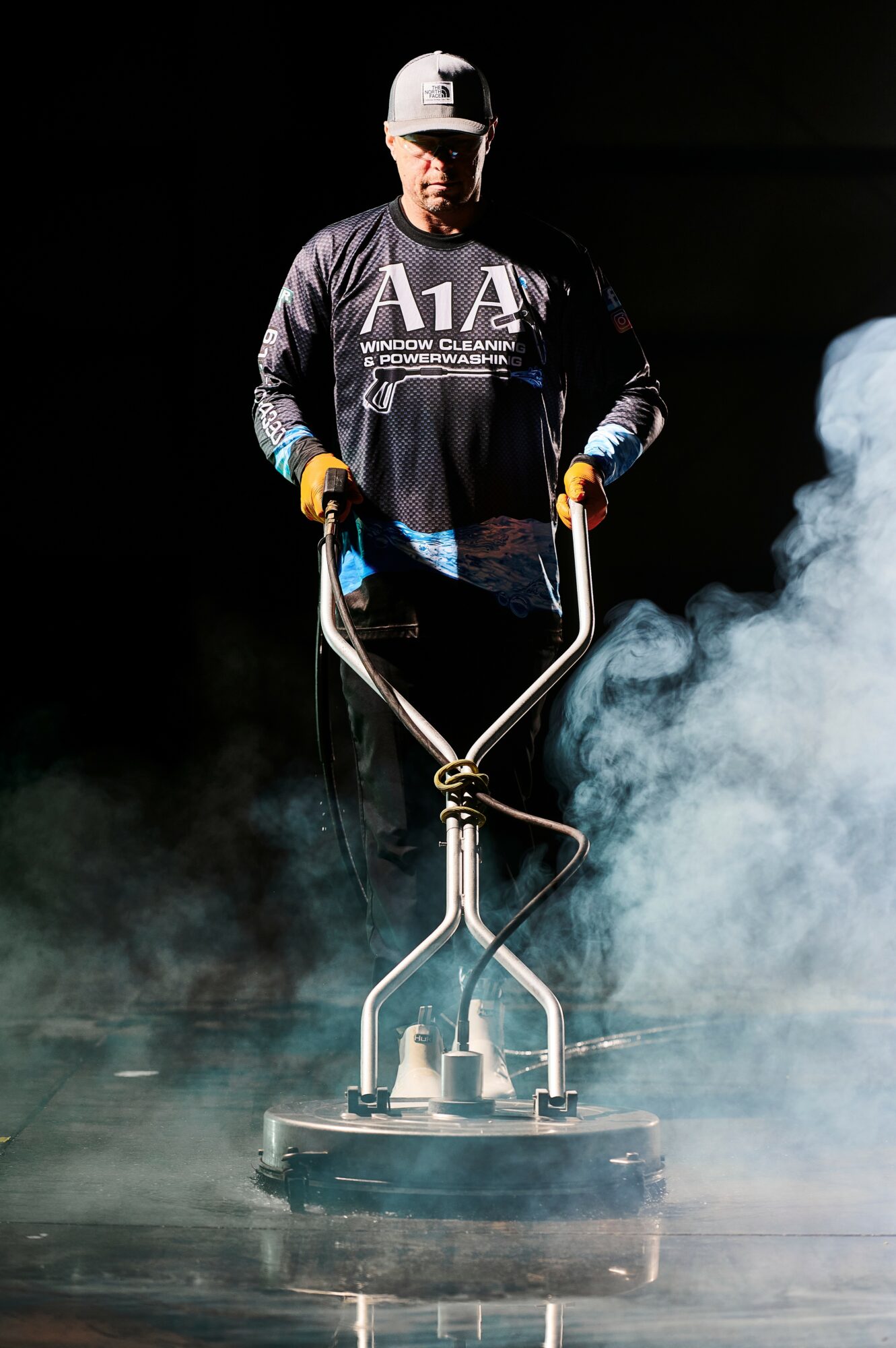 Person operating a floor polishing machine with smoke or steam around them, wearing a cap and dark clothing.