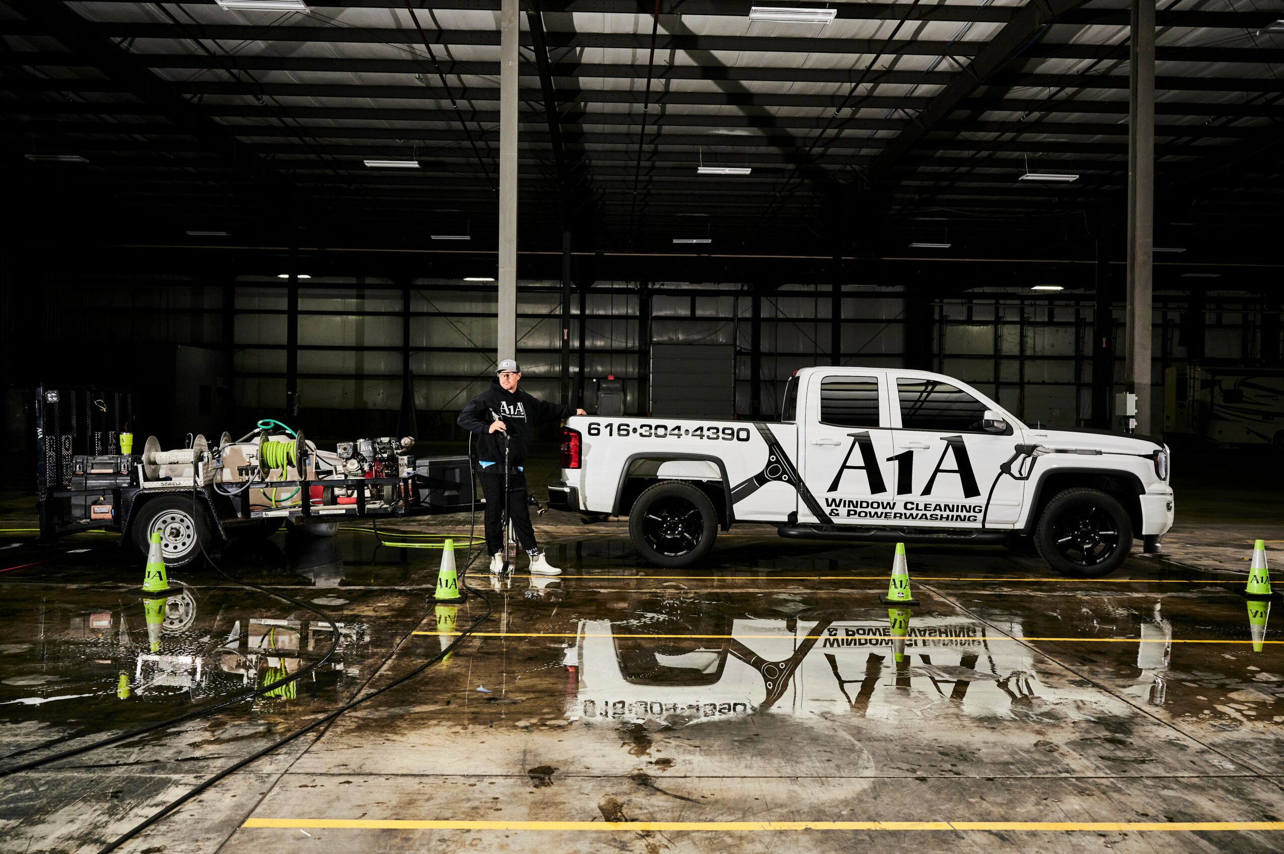 People and vehicles inside a large industrial building with wet floor reflections, safety cones, and a white pickup truck marked A1A.