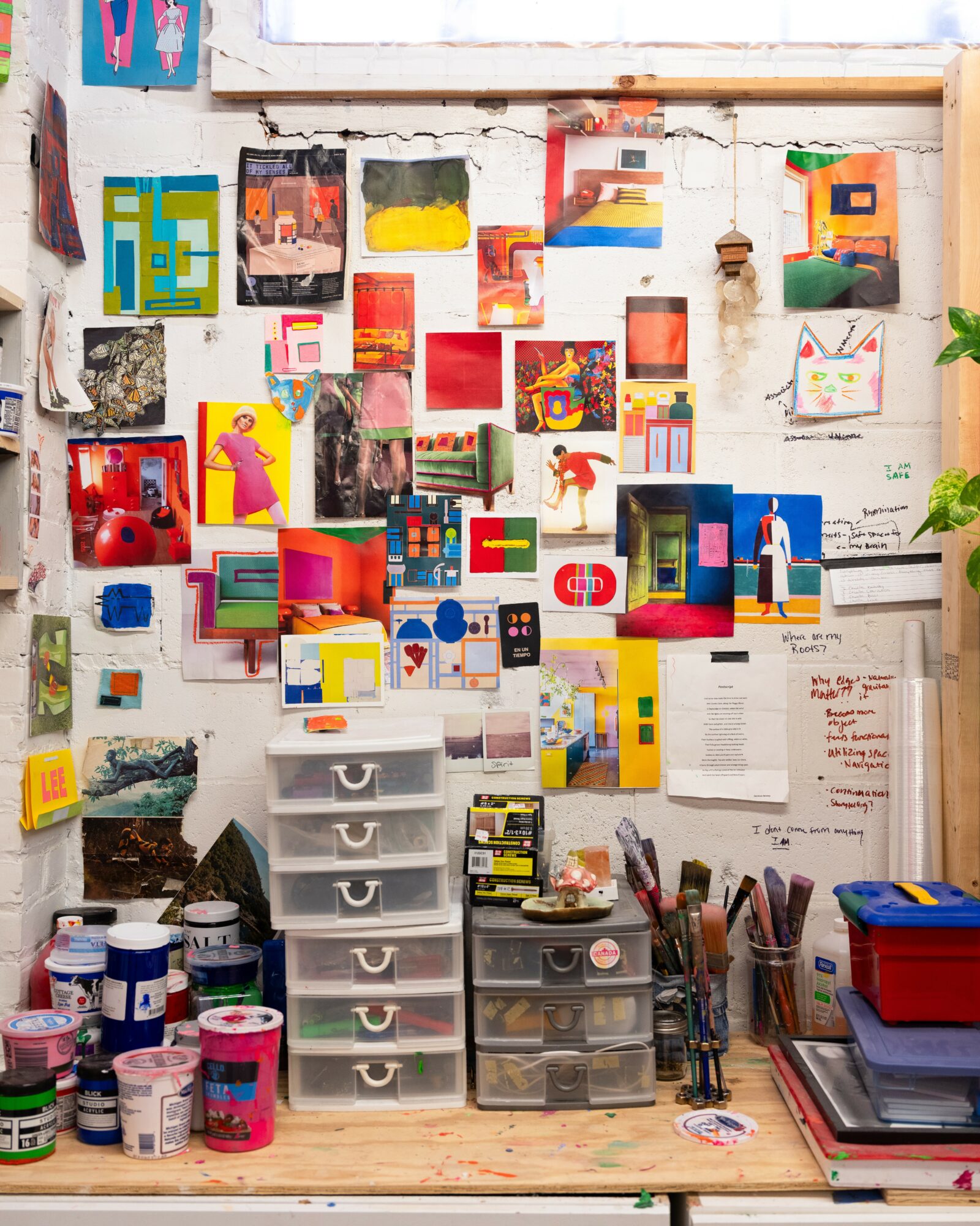 Wall with colorful abstract artwork, small hanging decorations, and a workspace with storage drawers, art supplies, and notebooks.