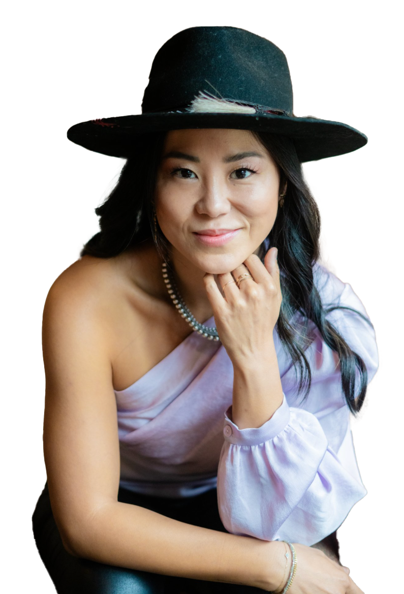 Woman wearing a black hat and pearl necklace, resting her chin on her hand, smiling, against a black background.