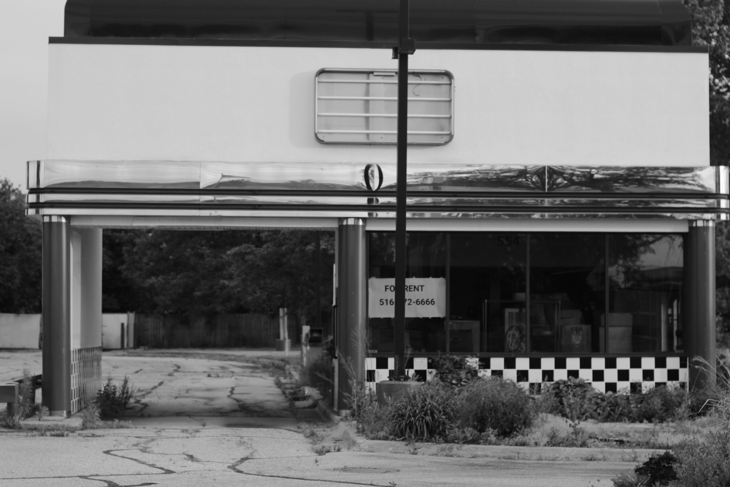 Building with a large window, striped awning, and checkered pattern at the bottom, surrounded by plants and trees.