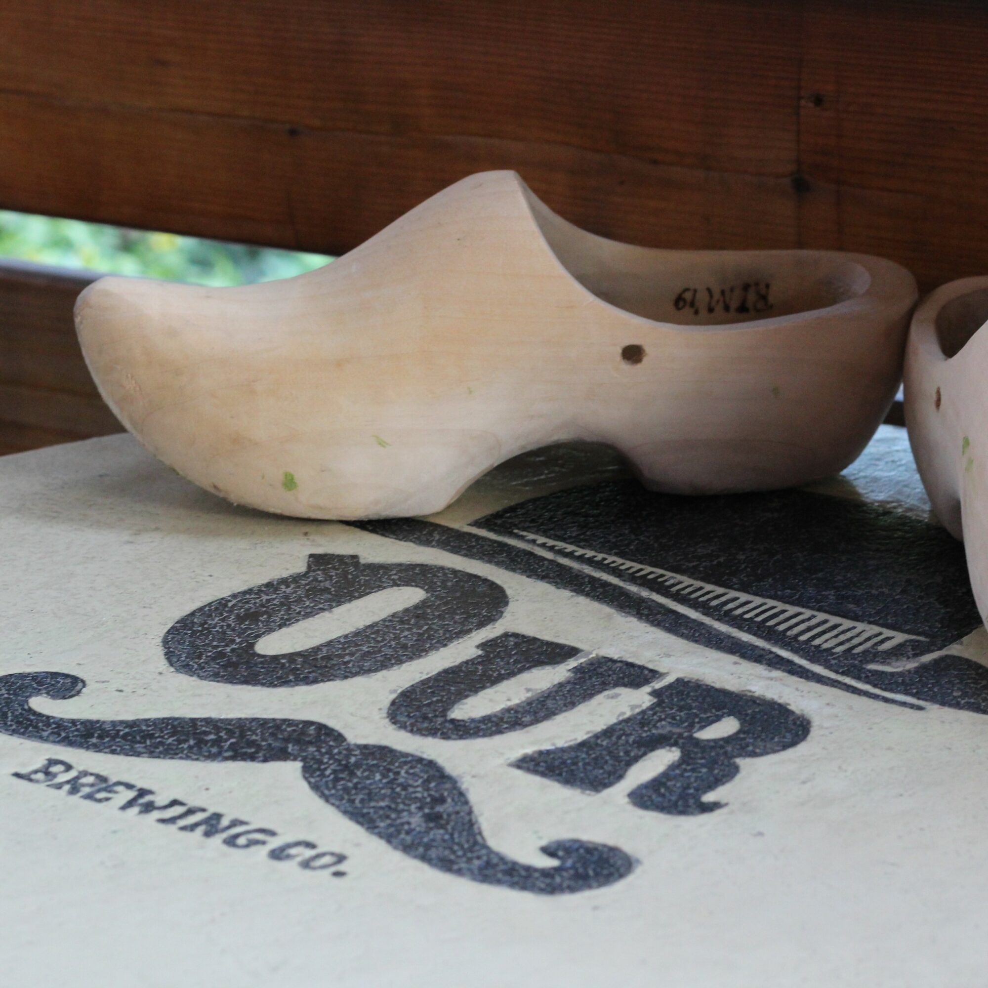 Wooden shoe-shaped object on a surface with text and a mustache graphic, against a wooden background.