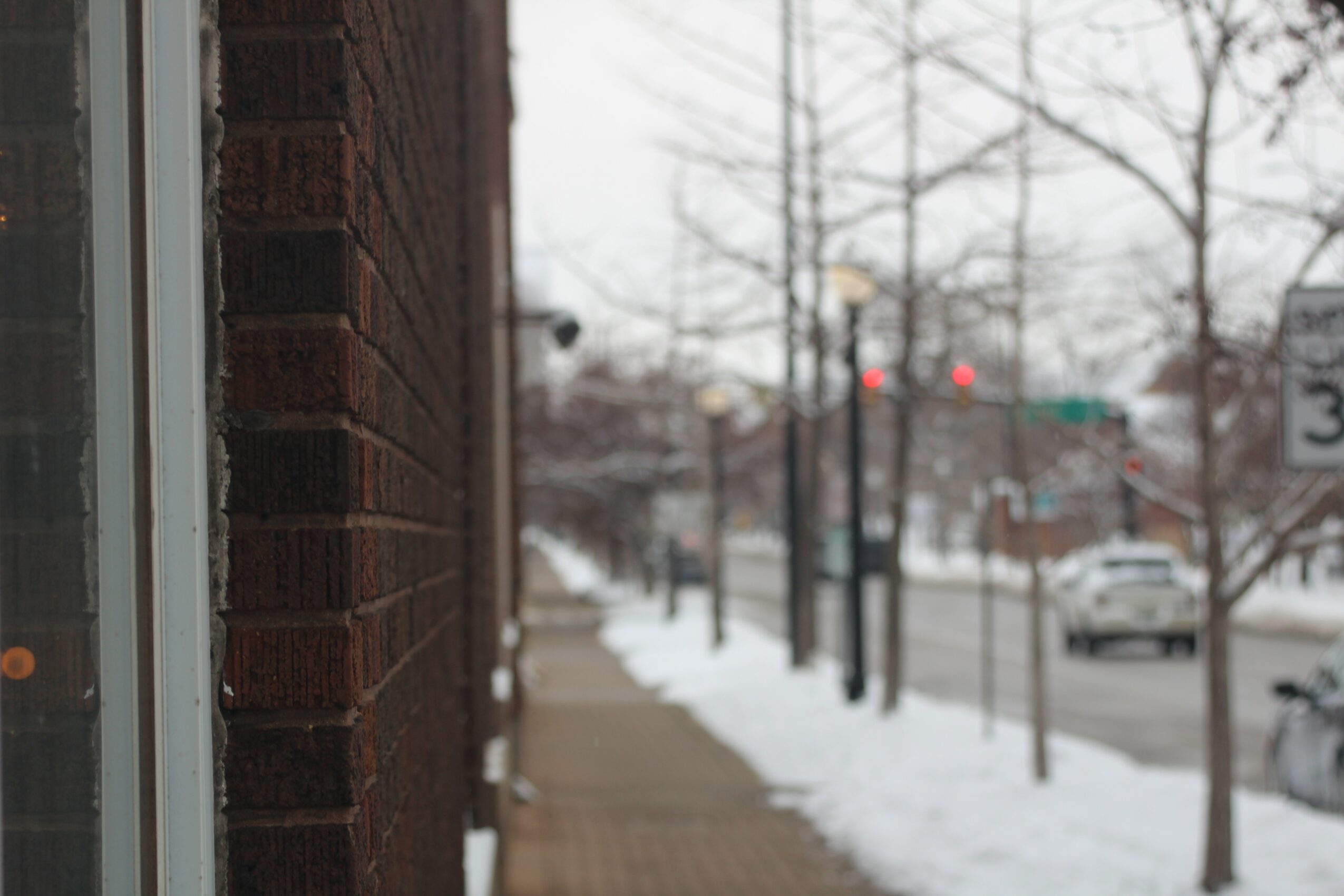 Side view of a brick building on a snowy sidewalk with trees and streetlights in the background.