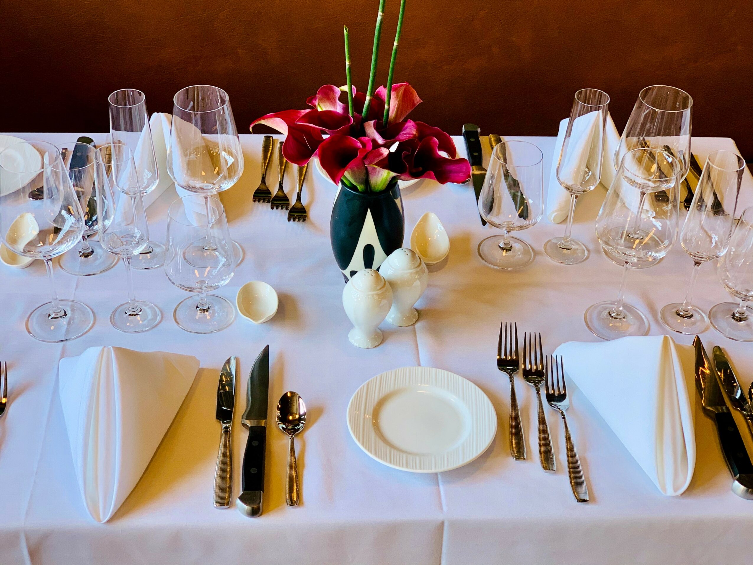 Table set with wine glasses, cutlery, white napkins, a floral centerpiece with red flowers, and decorative eggs.