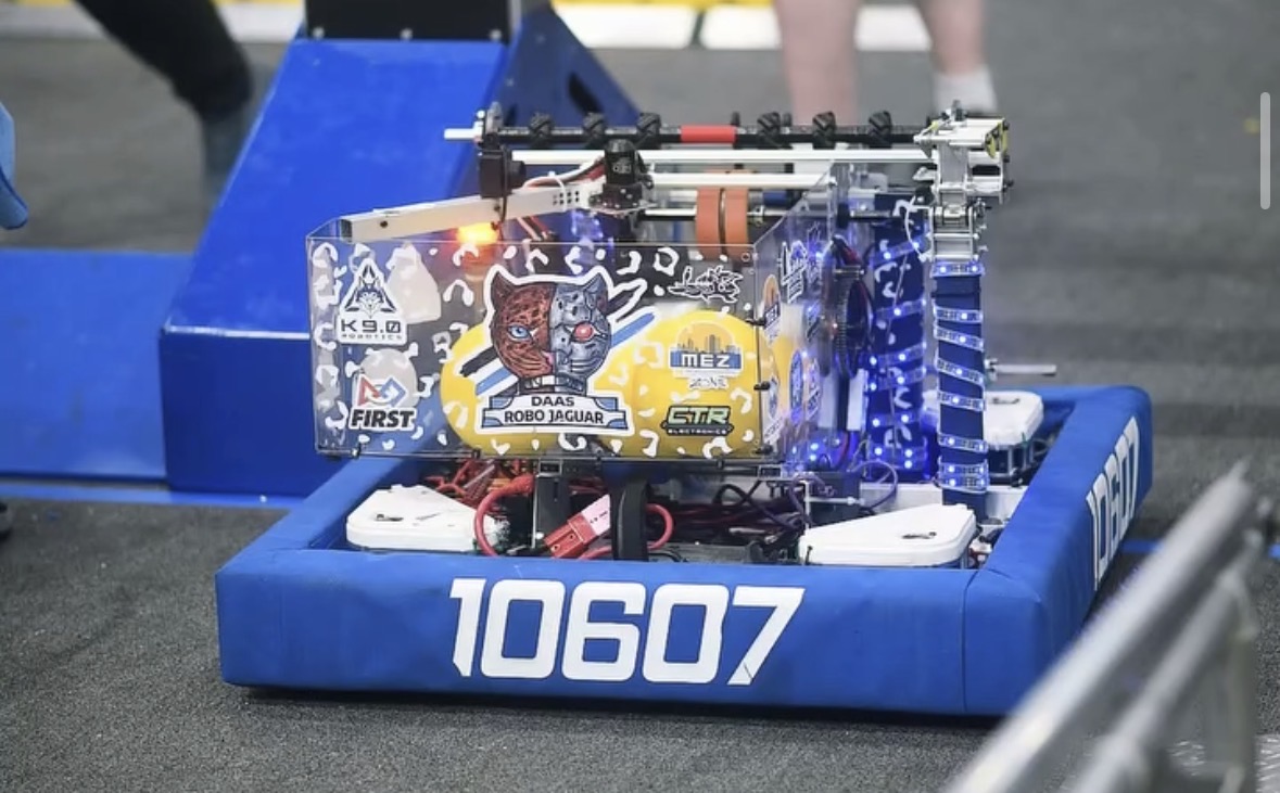 Robot with electronic components on a blue platform labeled 10607, at a robotics competition.