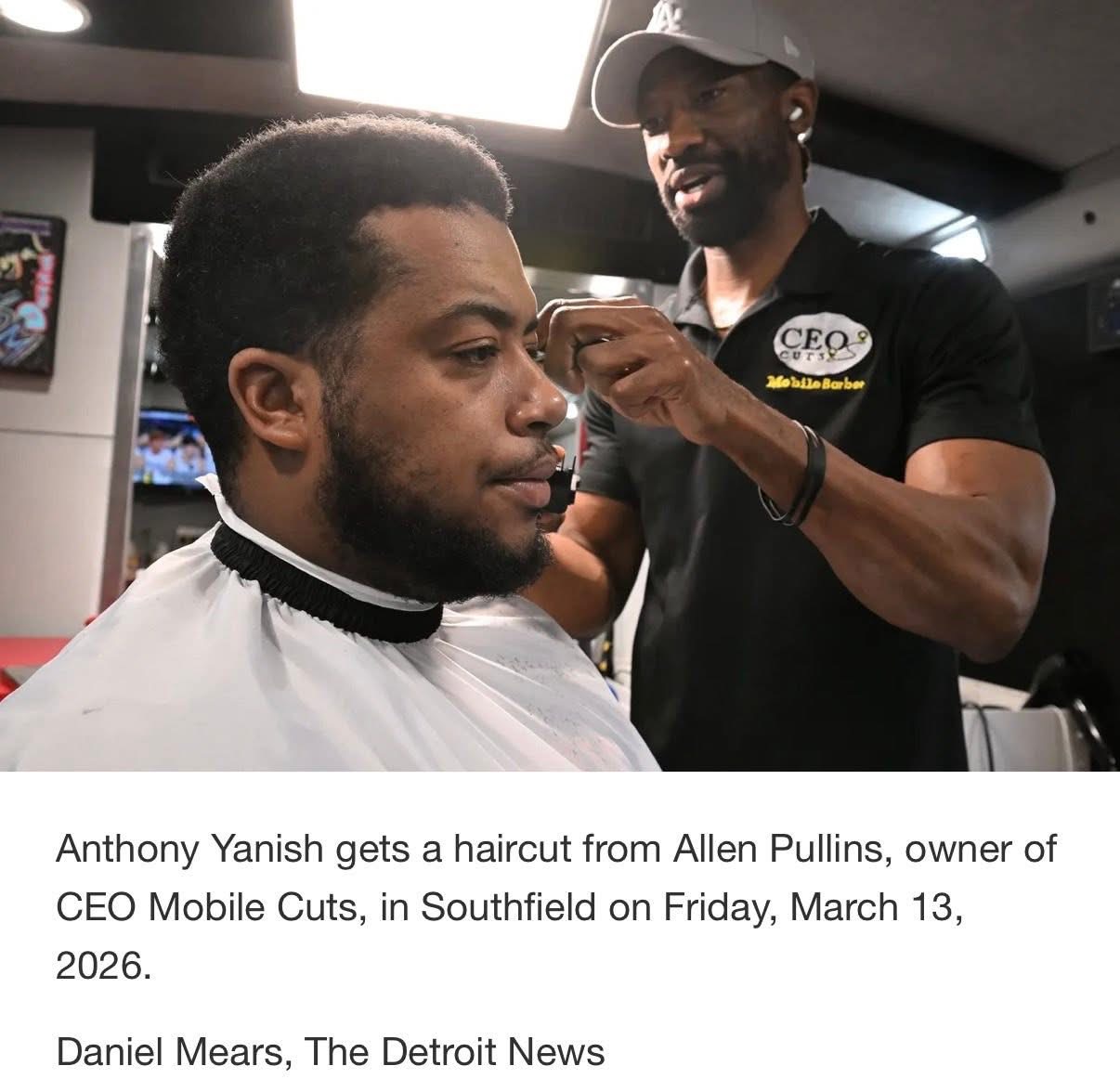 Man getting a haircut from barber in a salon, barber holding scissors, client with a cape, background with salon equipment.