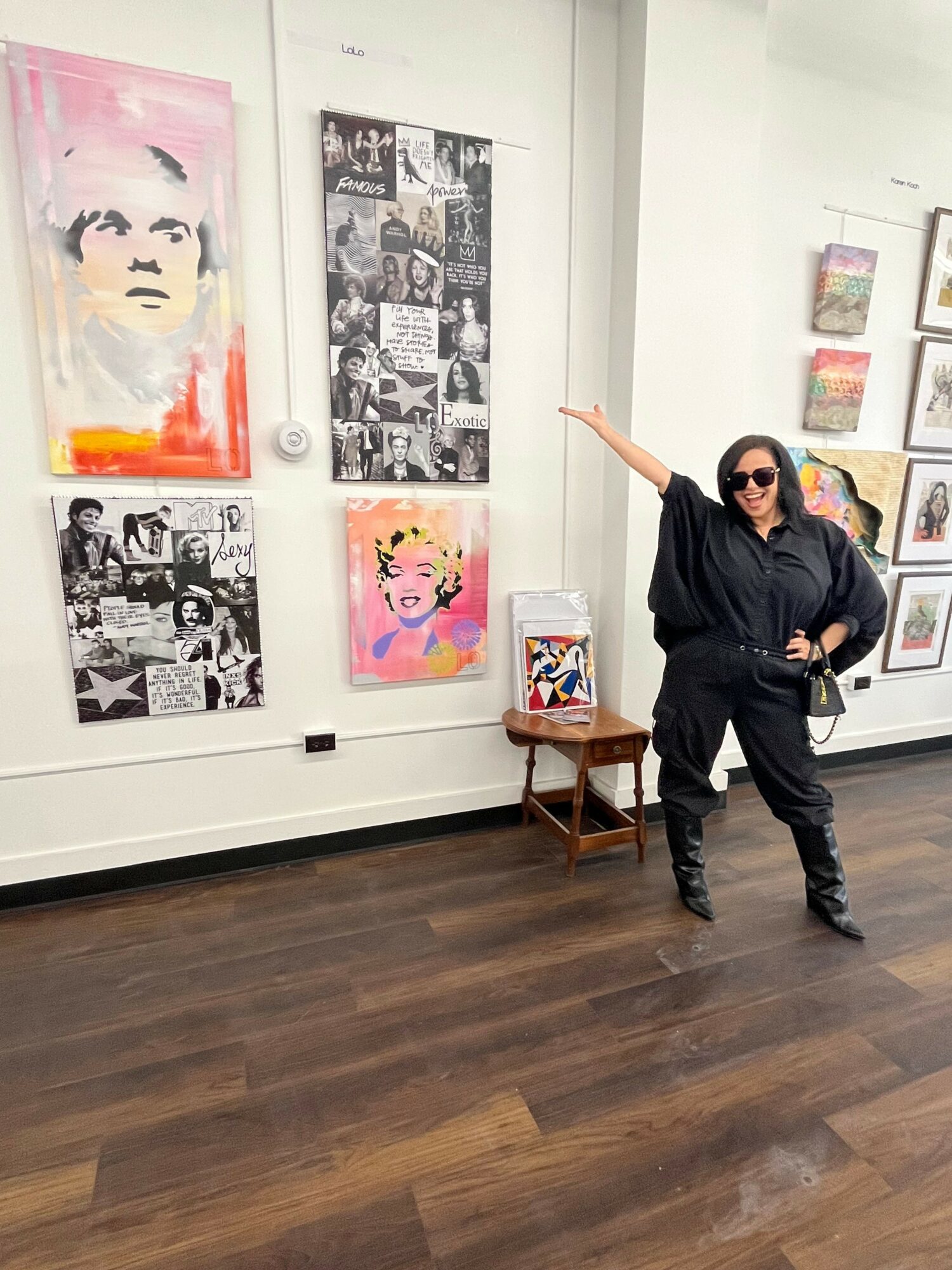 Person standing in an art gallery pointing at colorful artwork on the wall, with wooden floor and framed pictures.