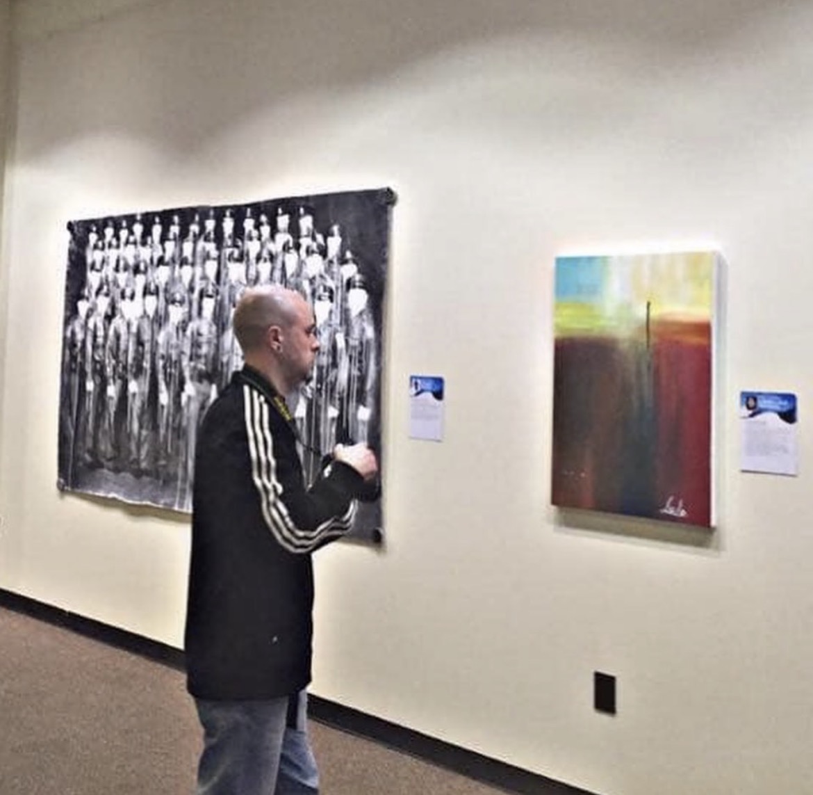 Person with glasses and black jacket looking at colorful abstract painting in gallery.