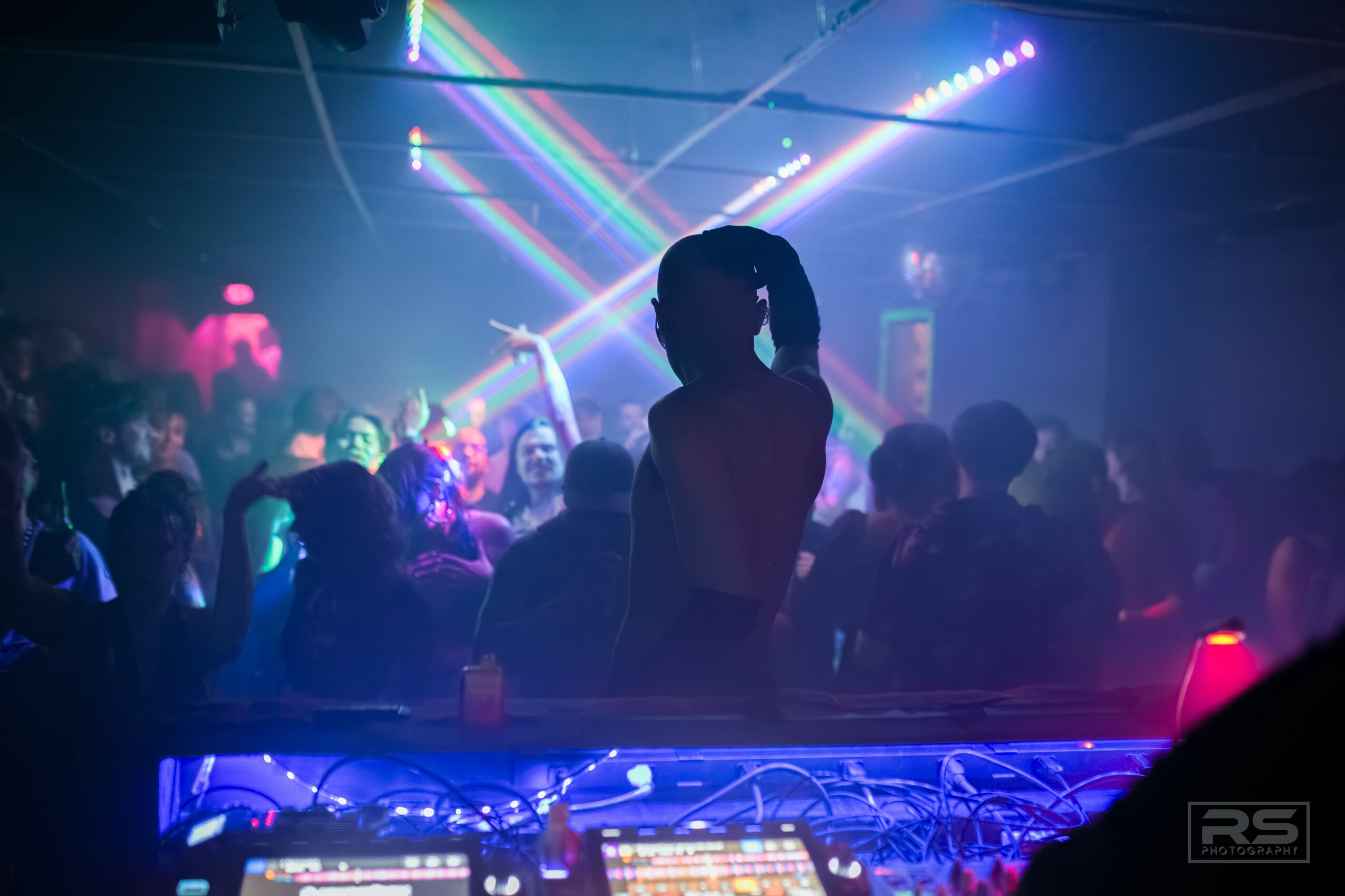 Silhouette of a person dancing in a club with colorful laser lights and a crowd in the background.