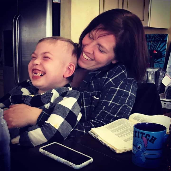 Woman and child laughing together, sitting at a table with a book, phone, and a blue cup with a cartoon character.