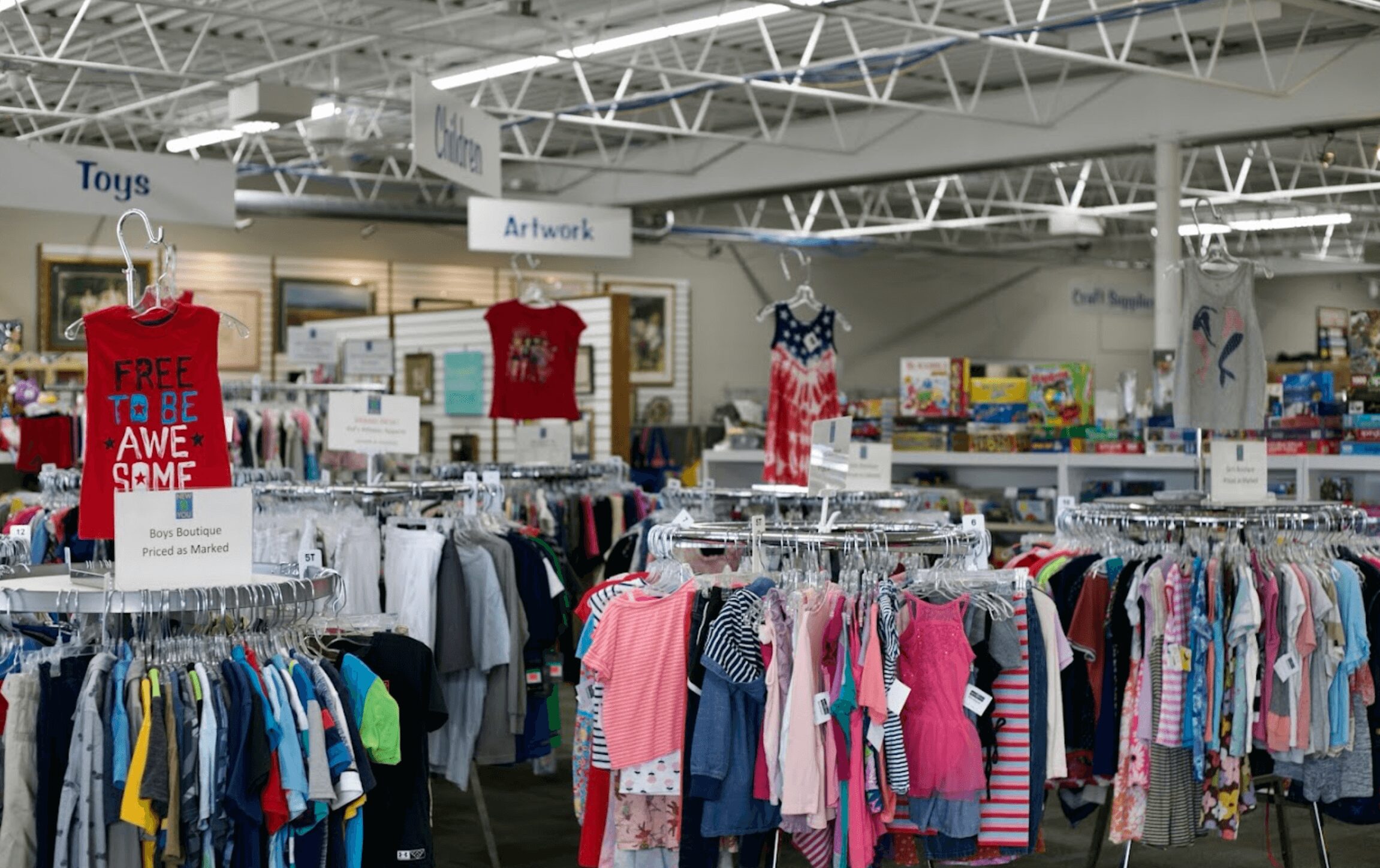 Clothing racks with children's and adult clothes inside a store, signs for toys and apparel visible in background.