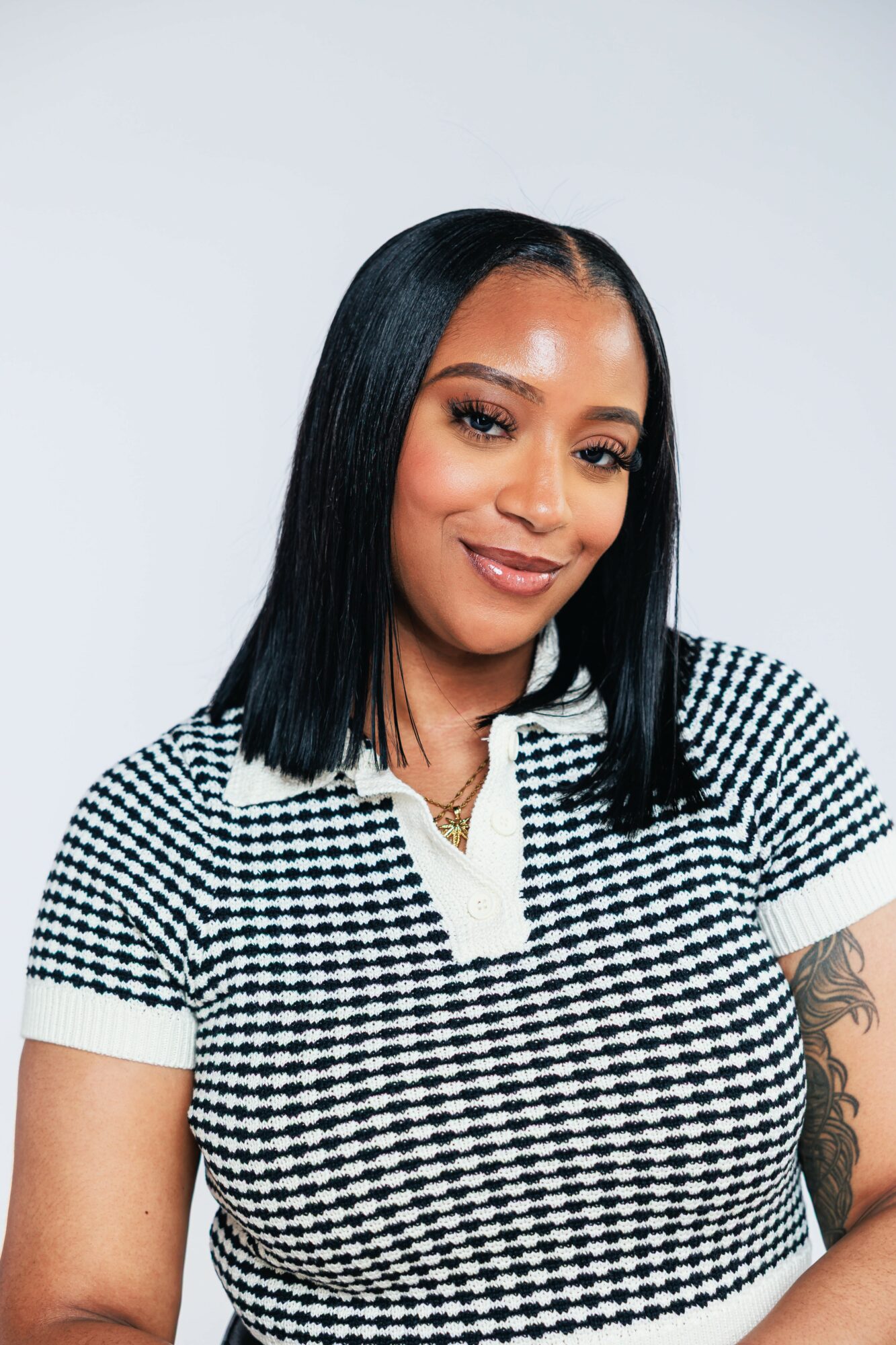 Woman with straight black hair wearing a black and white checkered top, smiling, against a plain background.