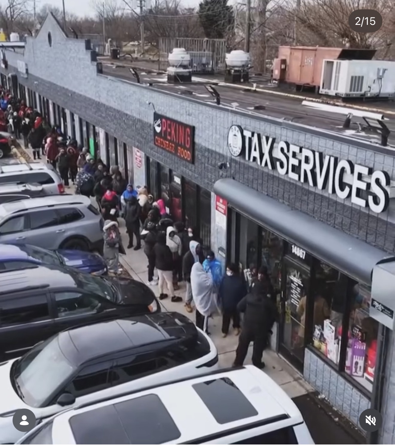 Line of people waiting outside a tax service store, parked cars in front, store sign visible, overcast day.