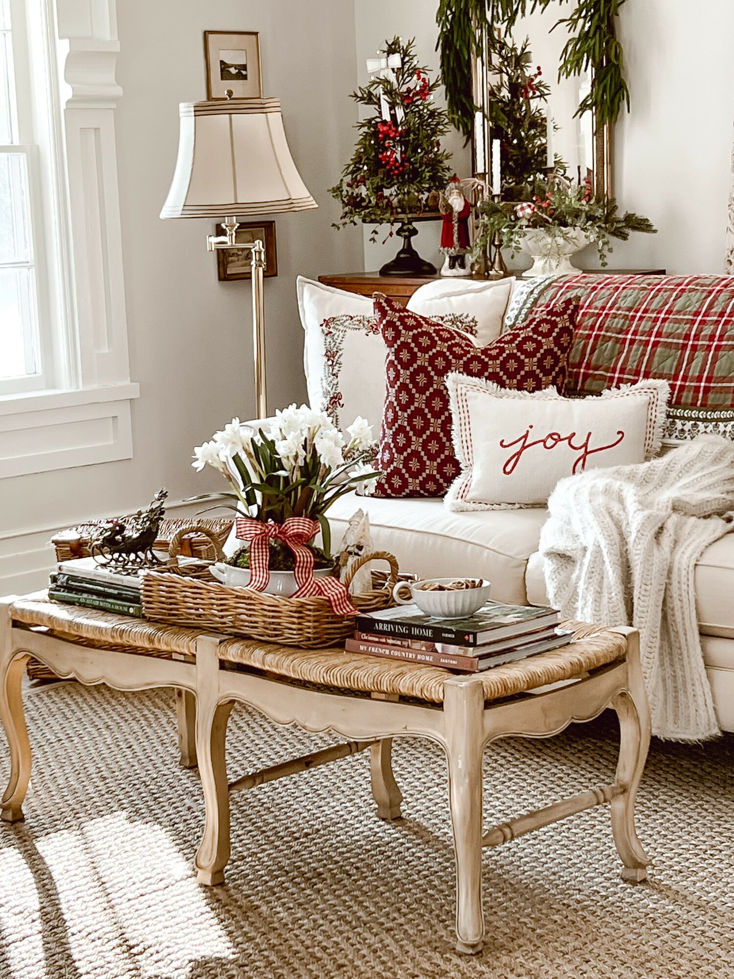 Living room with a white sofa, red and white pillows, a wooden coffee table, and a floral arrangement, decorated for Christmas.