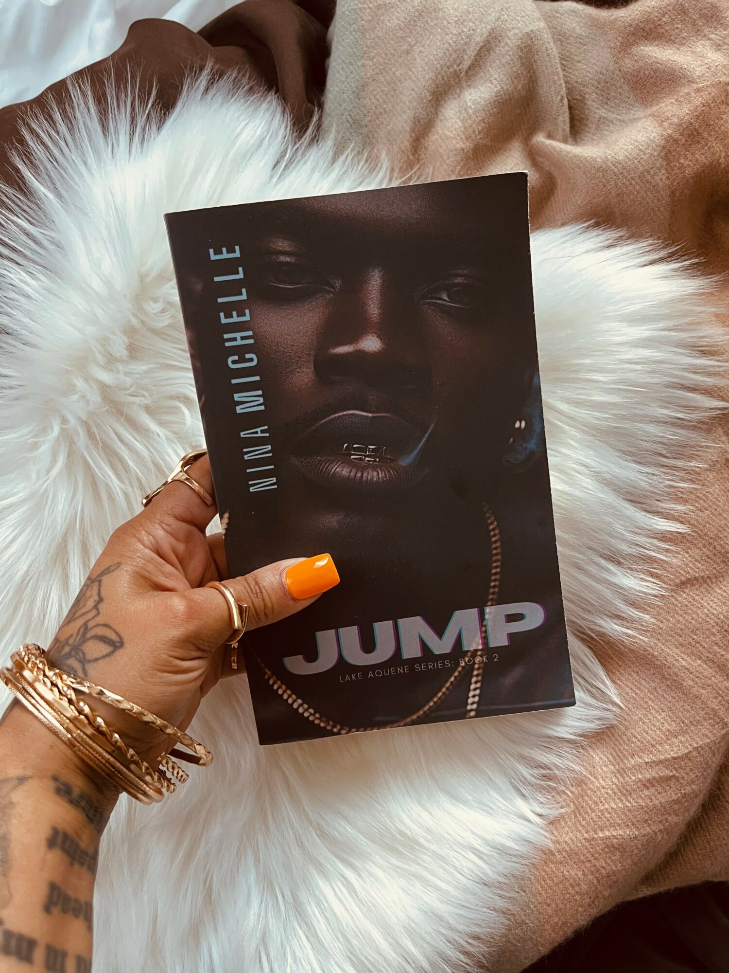 Person holding a book titled 'JUMP' with a dark-skinned woman's face on the cover, resting on a white furry surface.
